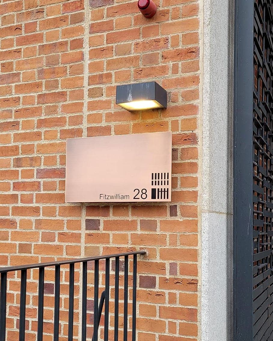 Brushed bronze entrance plaque at Fitzwilliam 28 for SMBC: a brick facade carrying a street address and number only, with no occupier name, security signage that identifies a building without disclosing what it holds