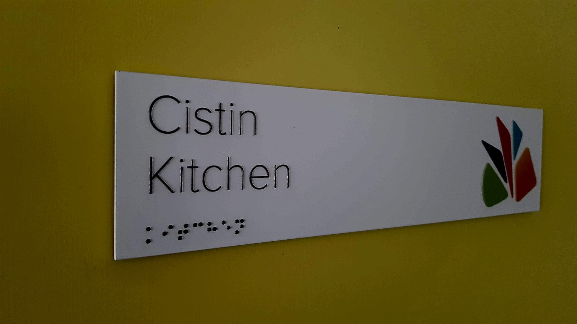 Bilingual Irish and English room sign reading Cistin / Kitchen with raised tactile lettering and braille: the baseline item in any signage package cost