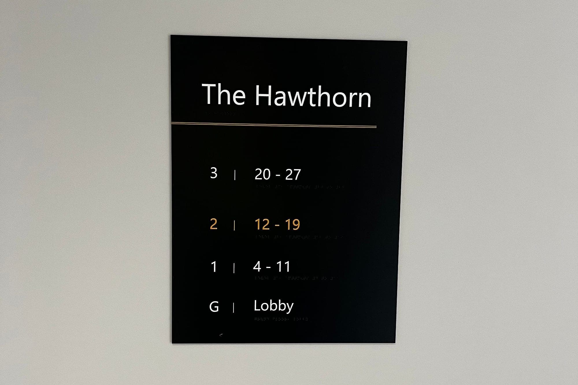 Build-to-rent signage at Churchfields, Swords: a residential block's level directory in white and amber on a matt black panel, listing each floor against its apartment-number range with braille beneath every line
