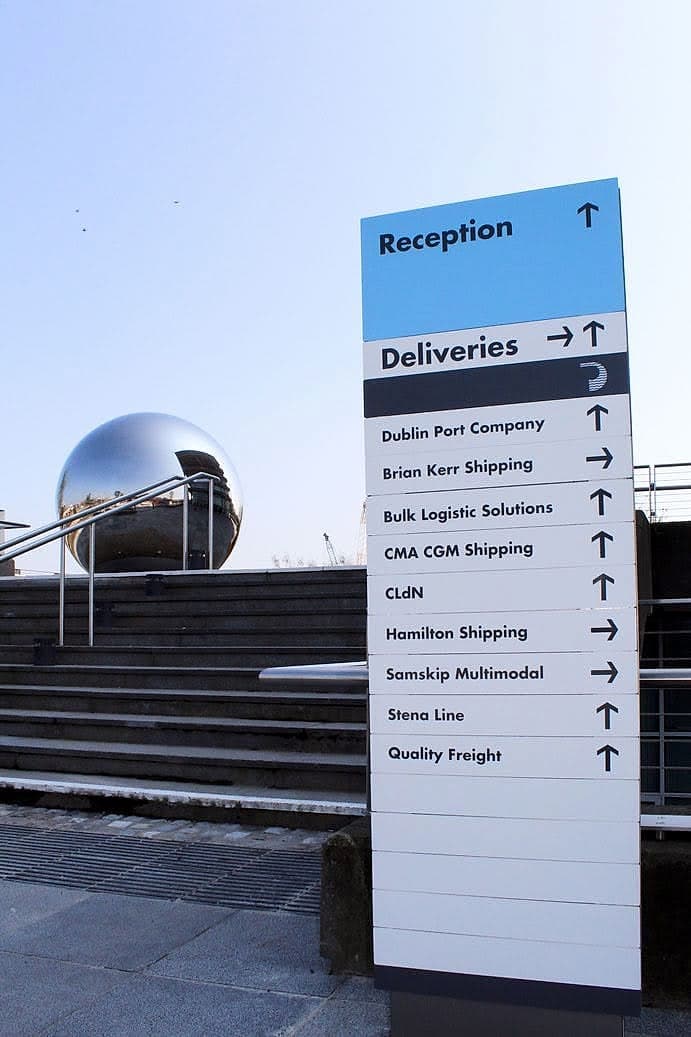 External wayfinding monolith at Dublin Port listing reception, deliveries and shipping tenants with directional arrows, ranked in a clear hierarchy