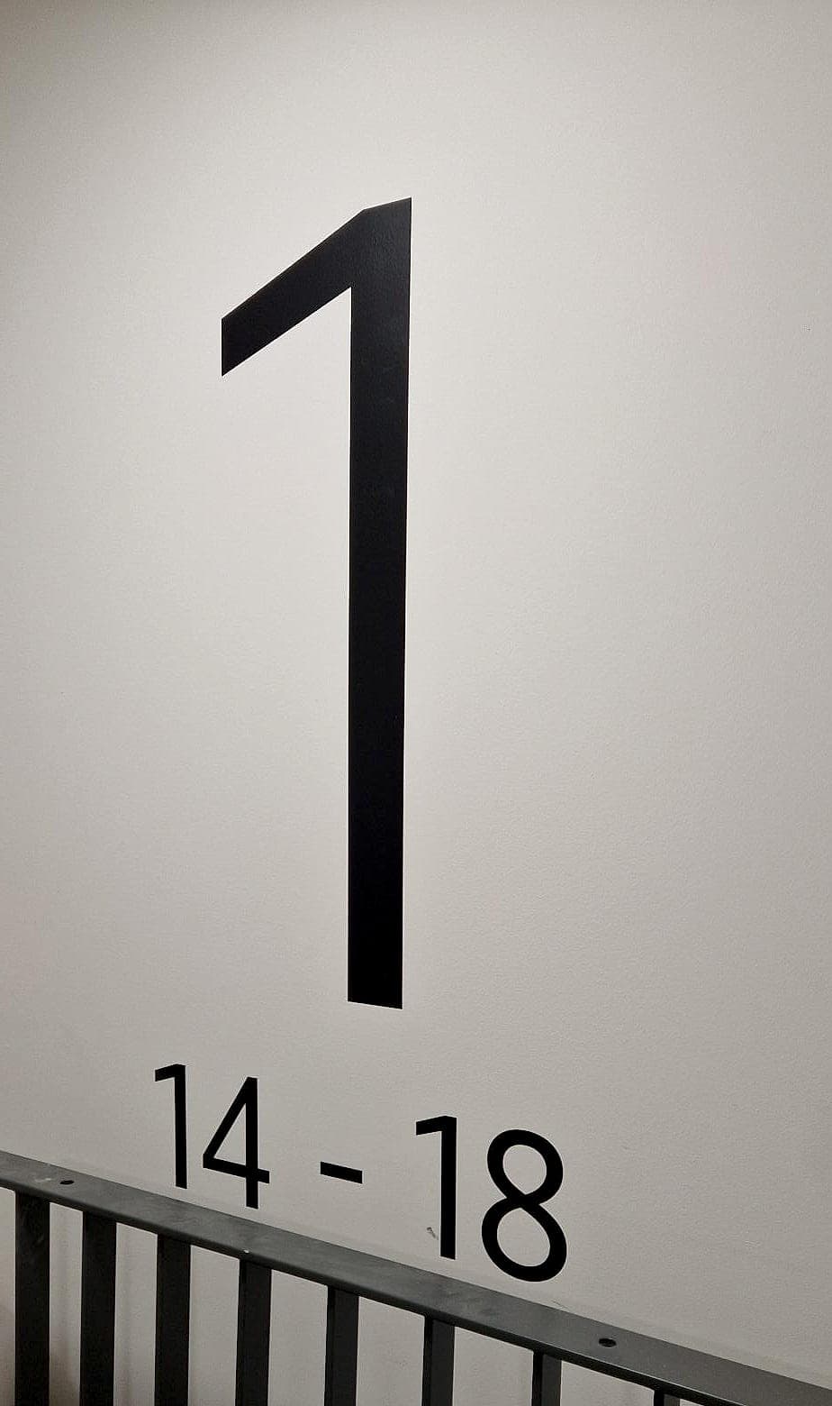 Signage colour contrast at Rathborne Wharf, Dublin: a large near-black level numeral one and apartment range 14–18 applied to a pale stair-core wall