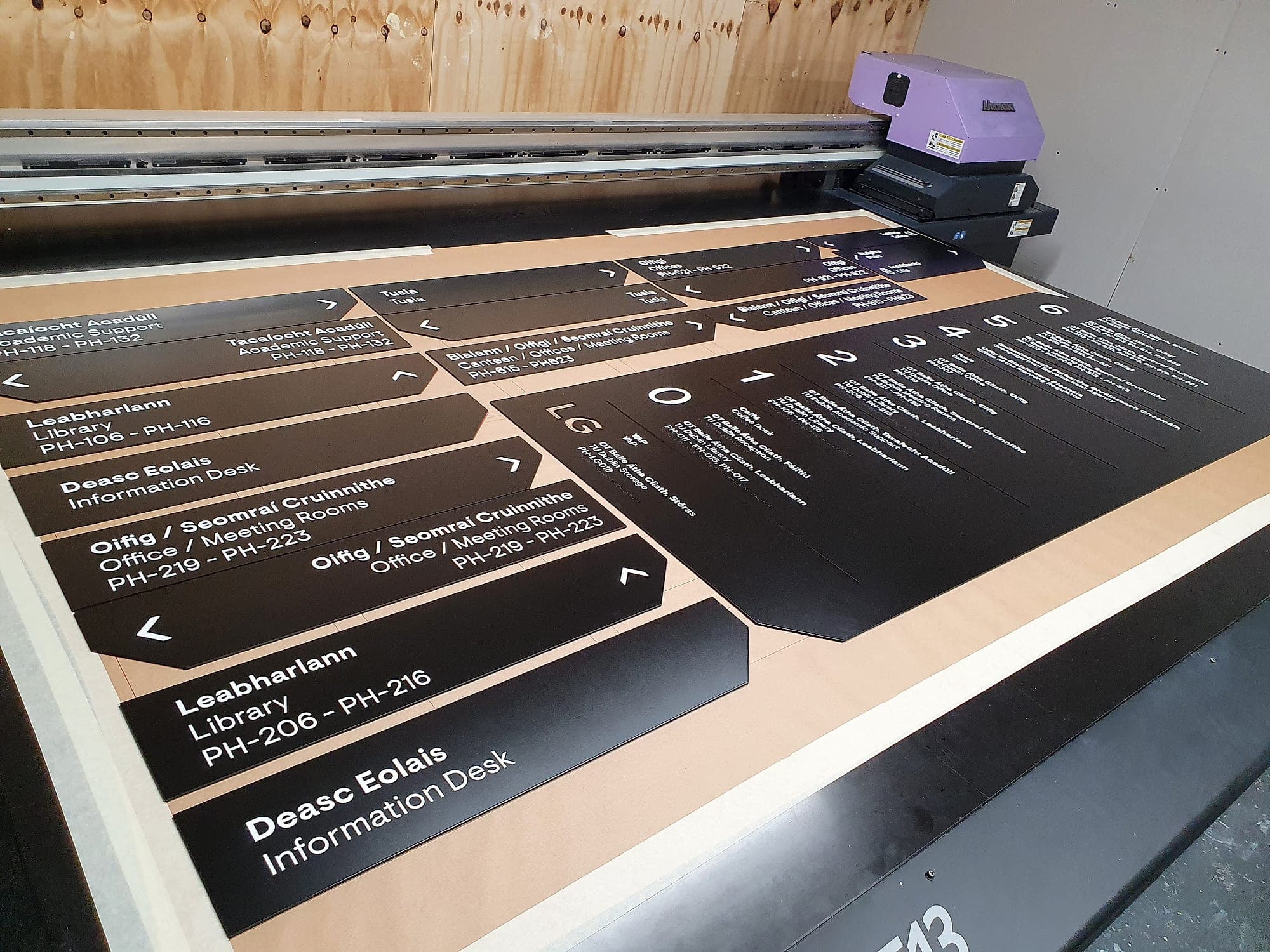 Internal signage system in production for Park House at TU Dublin: a bed of bilingual Irish and English directional panels printed in one run on a flatbed UV printer, each carrying room-number ranges