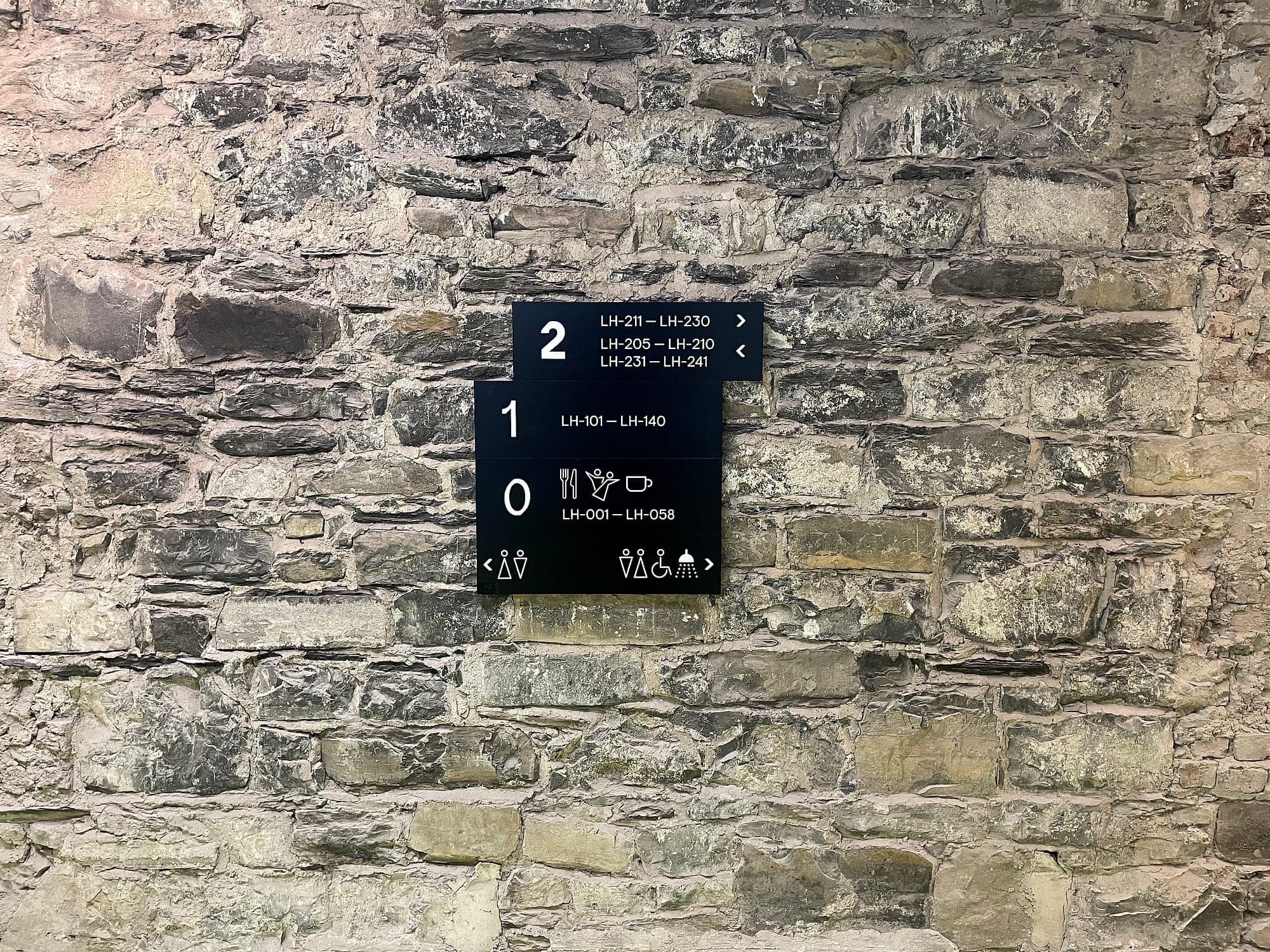 Listed building signage: a compact stepped floor directory in dark grey and white fixed to a rubble limestone wall in a historic building