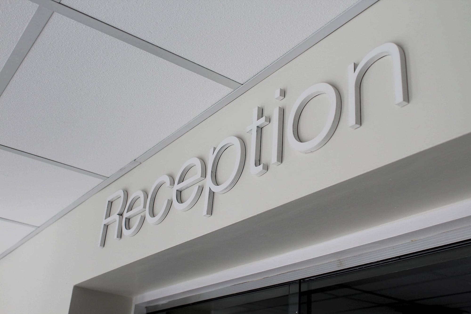 Newcastle West Primary Care Centre: built-up mixed-case lettering spelling Reception mounted above an entrance, seen from below, with generous x-height and open counters in wayfinding typography