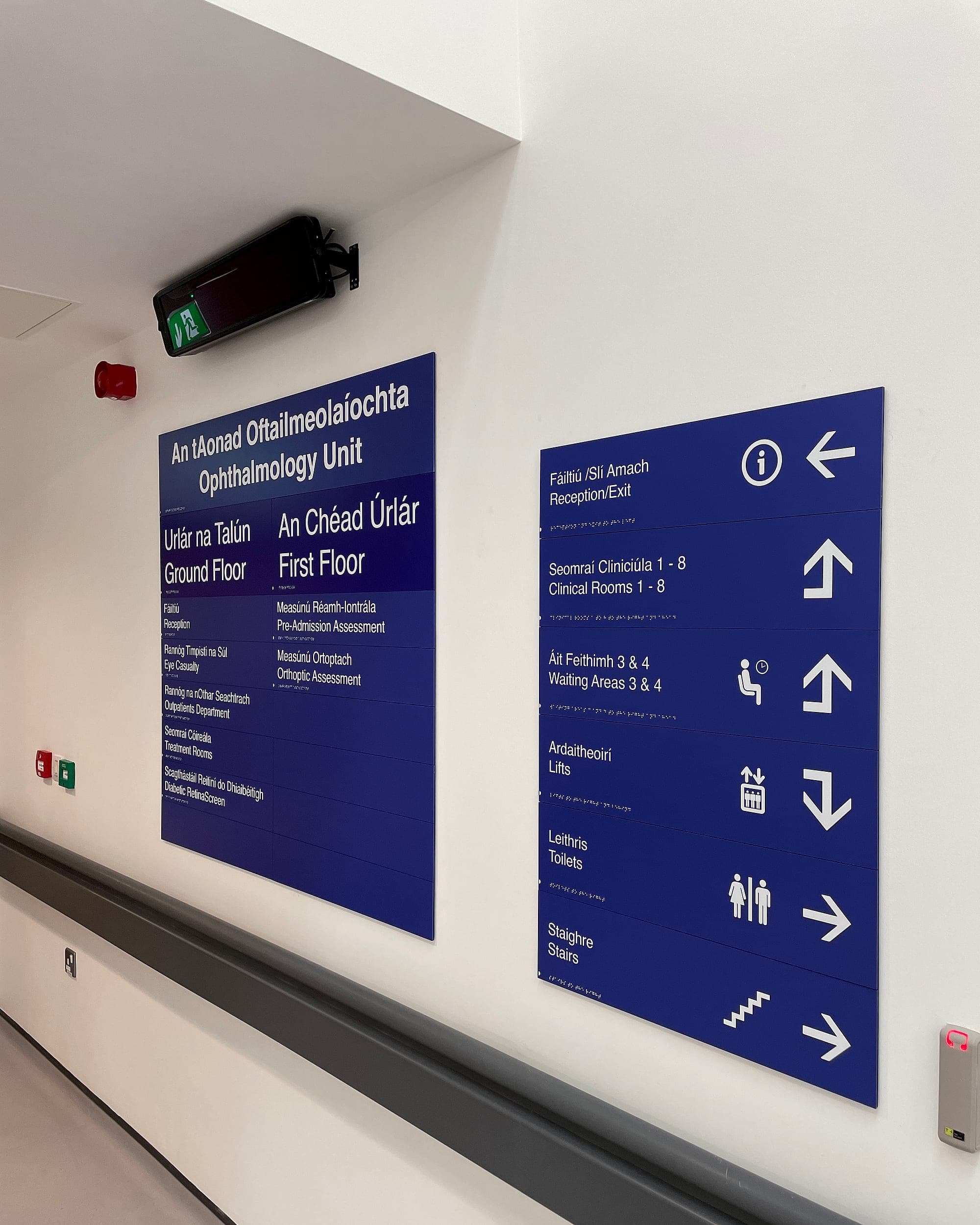 South Infirmary Victoria University Hospital: bilingual hospital directional signs in an ophthalmology unit, every destination anchored by a pictogram and braille, in one repeated format