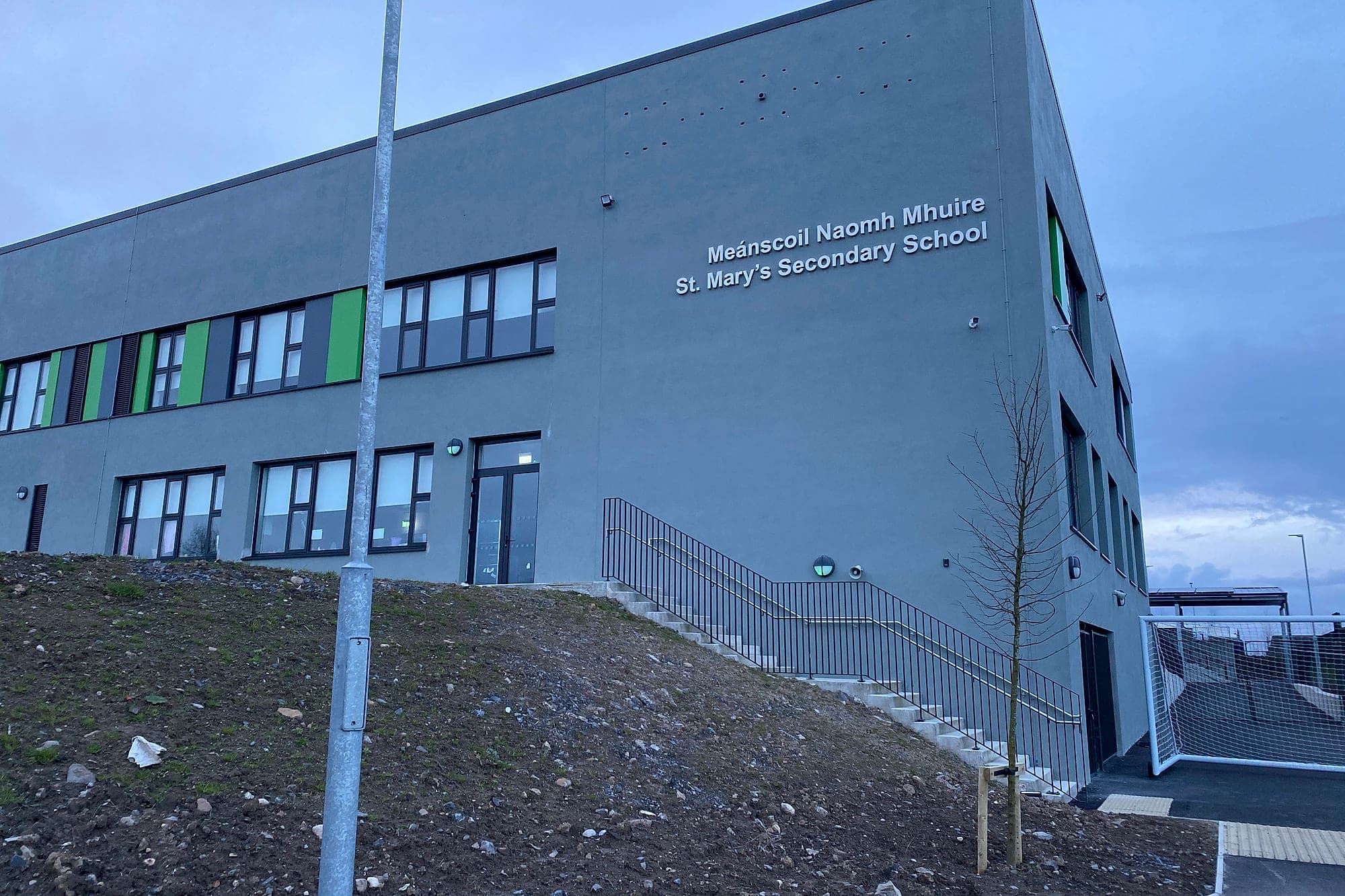 A new secondary school for the Department of Education: bilingual Irish and English built-up building identification lettering on the render of a newly completed secondary school, with the site still unlandscaped below