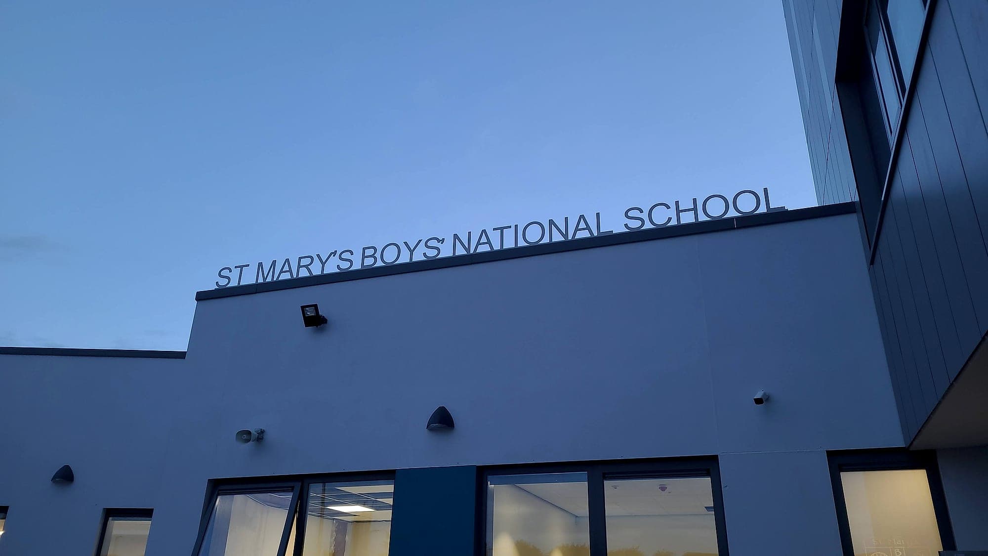 School signage in Ireland: built-up lettering reading St Mary's Boys' National School along the parapet of the new school building at Ennistymon Education Campus at dusk