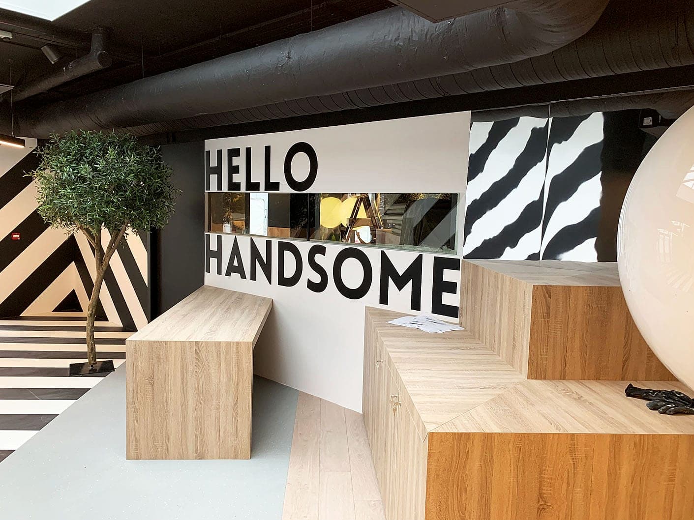 Student accommodation signage at Hatch: oversized HELLO HANDSOME wall lettering above the reception bench, with black and white chevron floor and wall graphics