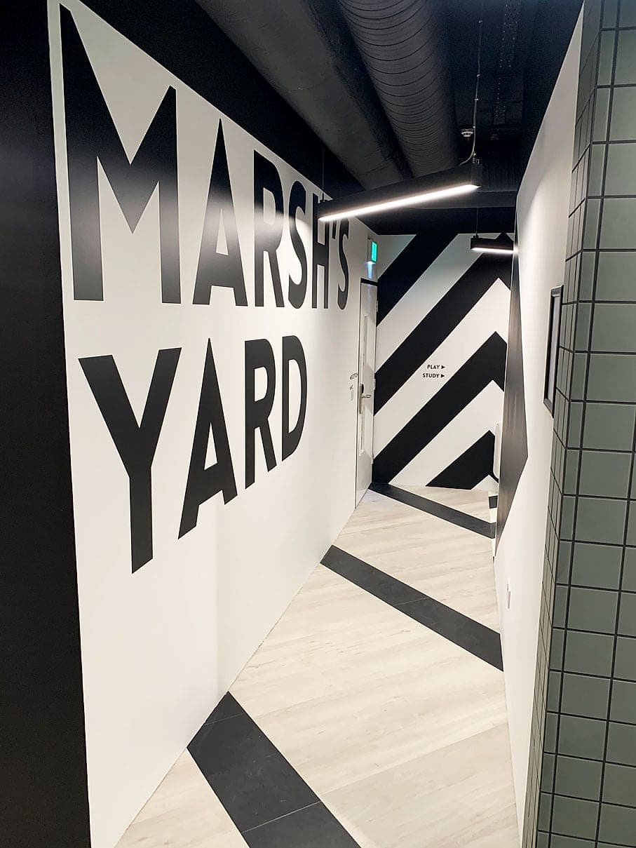 Supergraphic wall naming Marsh's Yard at Hatch Student Accommodation, Dublin: metre-high black lettering with chevron wall and floor graphics carrying movement through the corridor