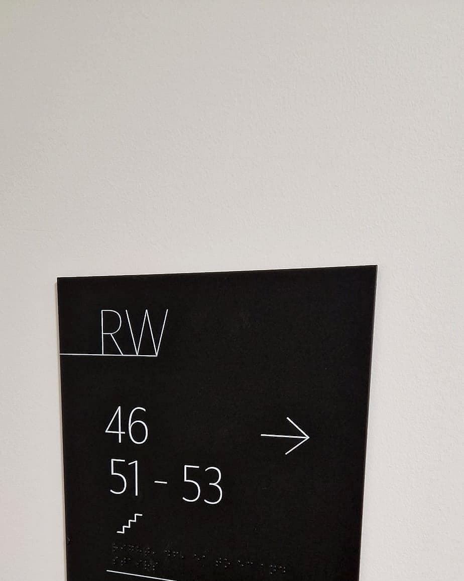 Accessible signage certification in practice: tactile level identification sign with raised numerals and braille on a matt black panel at Rathborne Wharf, Dublin
