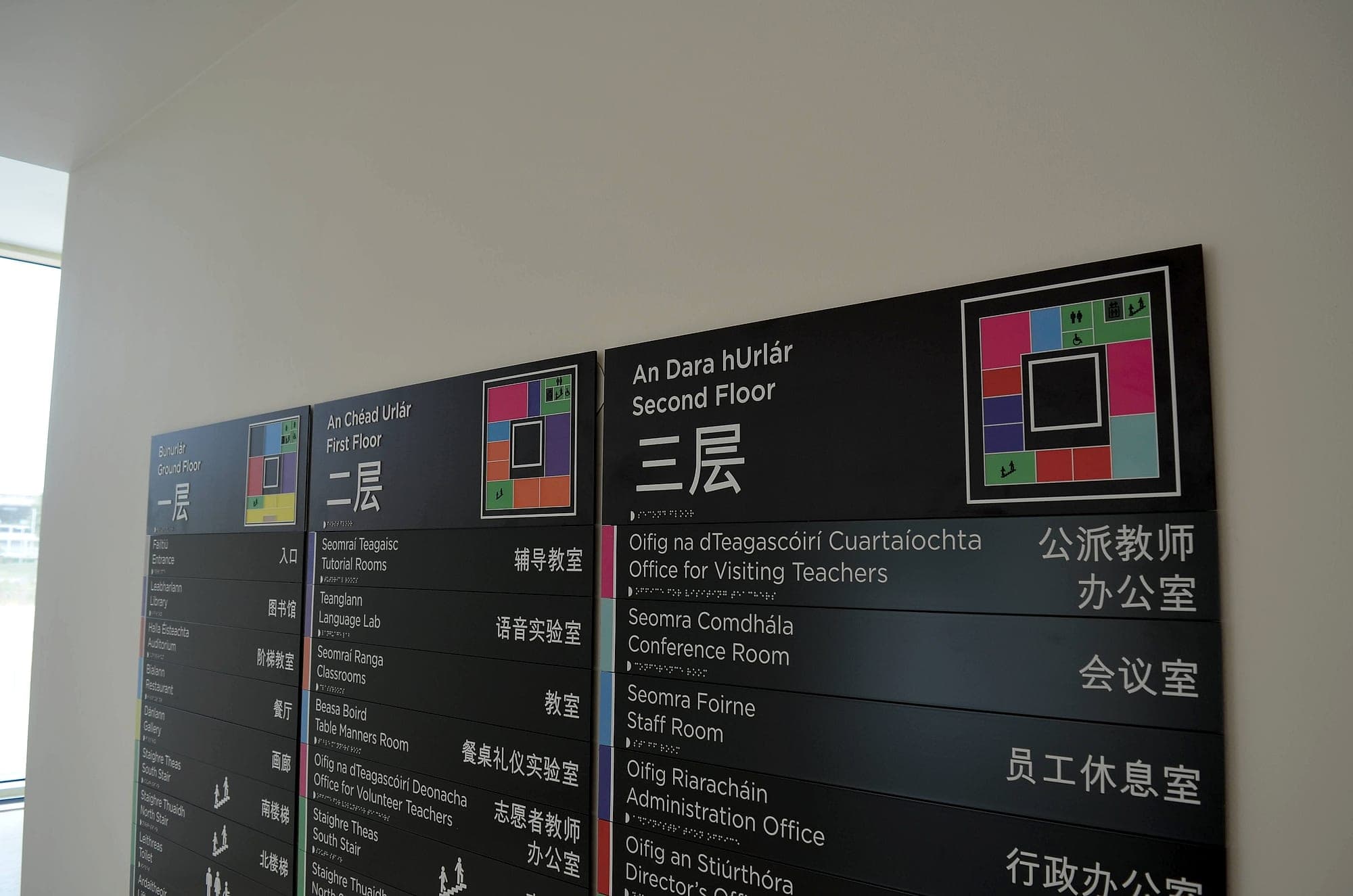 Trilingual floor directory signage in Irish, English and Chinese at the Confucius Institute: three wall-mounted slatted directory panels with braille strips and colour-coded floor plan keys