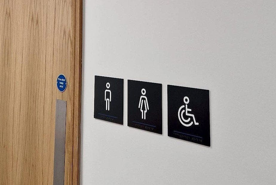 Tactile toilet signage with braille mounted at hand height beside the leading edge of a door at CCT College Dublin
