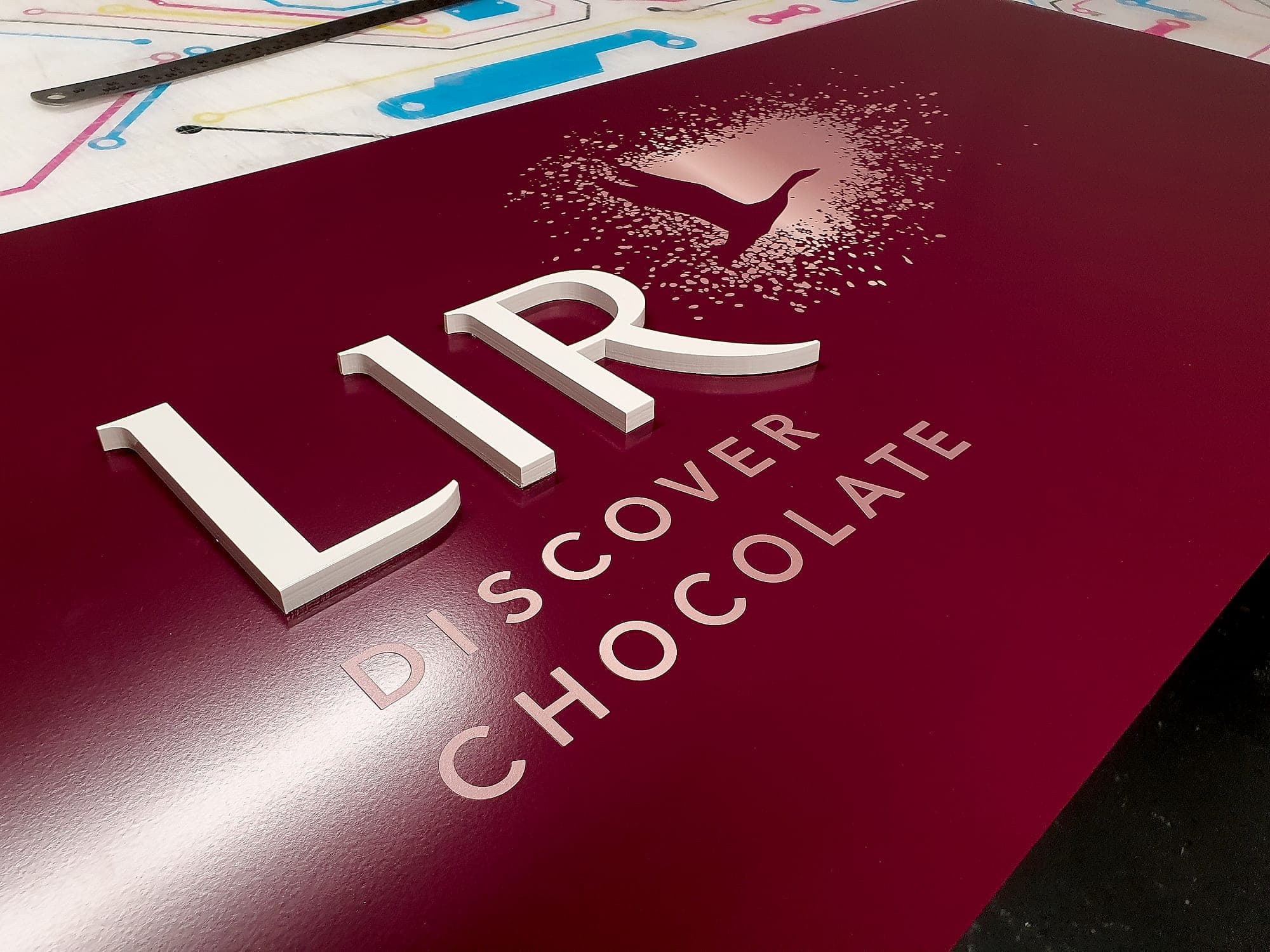 Signage materials in the workshop: flat-cut acrylic letters laid on a printed panel on the bench, cut edges showing the full thickness of the solid material