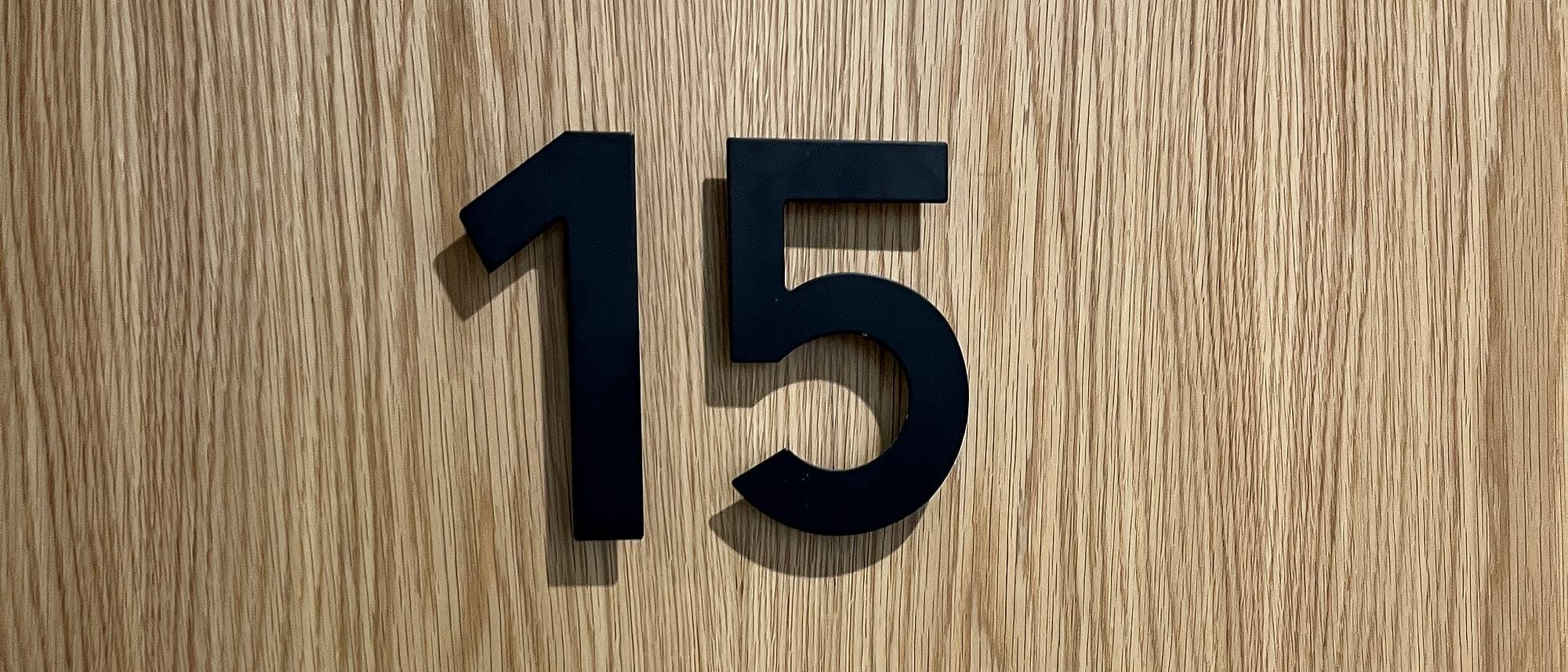Apartment door number signage: an individual cut satin-black numeral 15 face-fixed to an oak veneer apartment entrance door