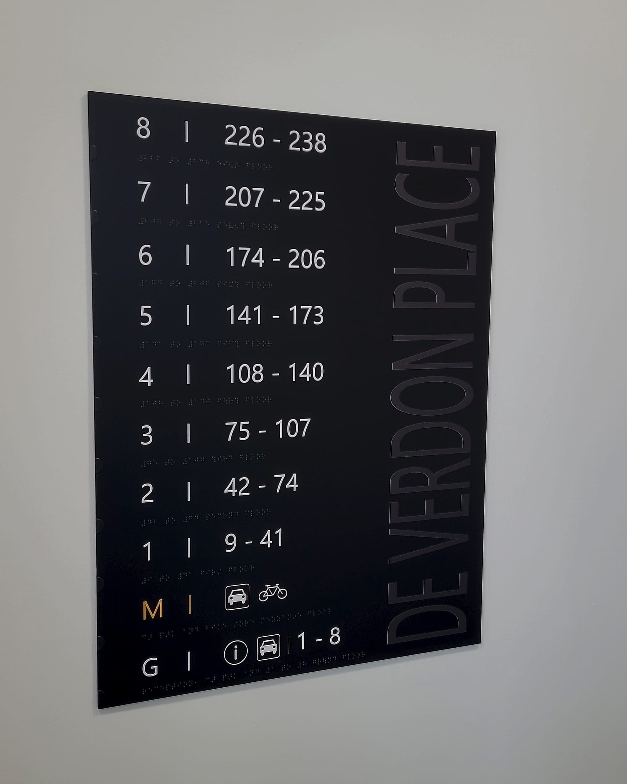 Residential internal signage directory at De Verdon Place, Clarehall, listing floors against apartment-number ranges, with tactile lettering and braille beneath each line