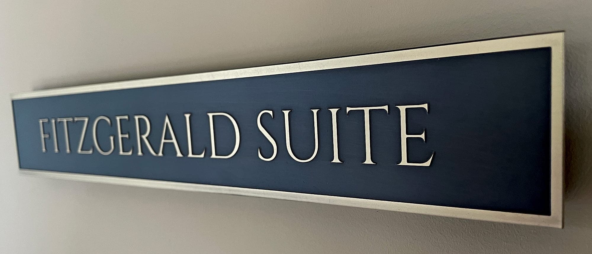 Bespoke routed suite name sign at Carton House, with raised metallic lettering on a two-tone blue panel with a brushed metal border, mounted on a plain wall