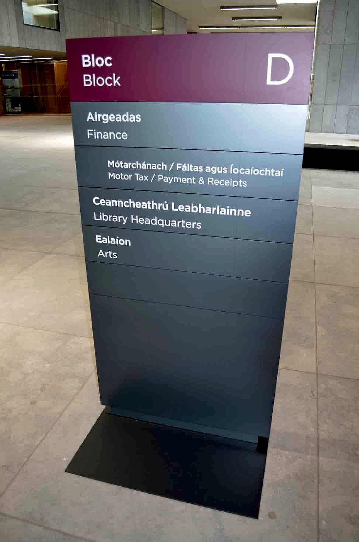 Freestanding bilingual directory monolith for Block D at Wexford County Council headquarters, listing Finance, Motor Tax, Library Headquarters and Arts in Irish and English