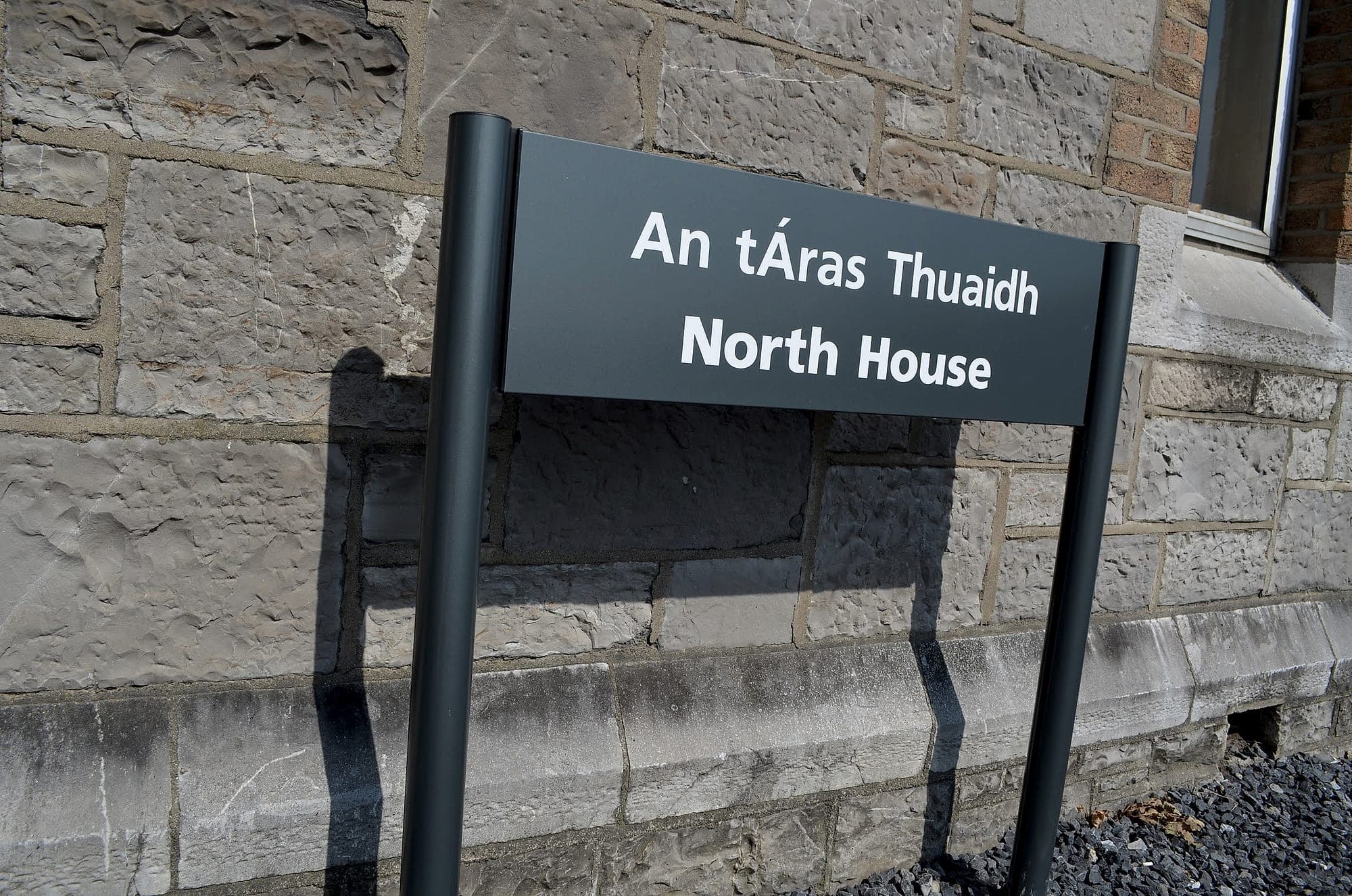 Grangegorman: bilingual Irish and English building identification sign on twin posts standing in front of a cut-stone historic facade