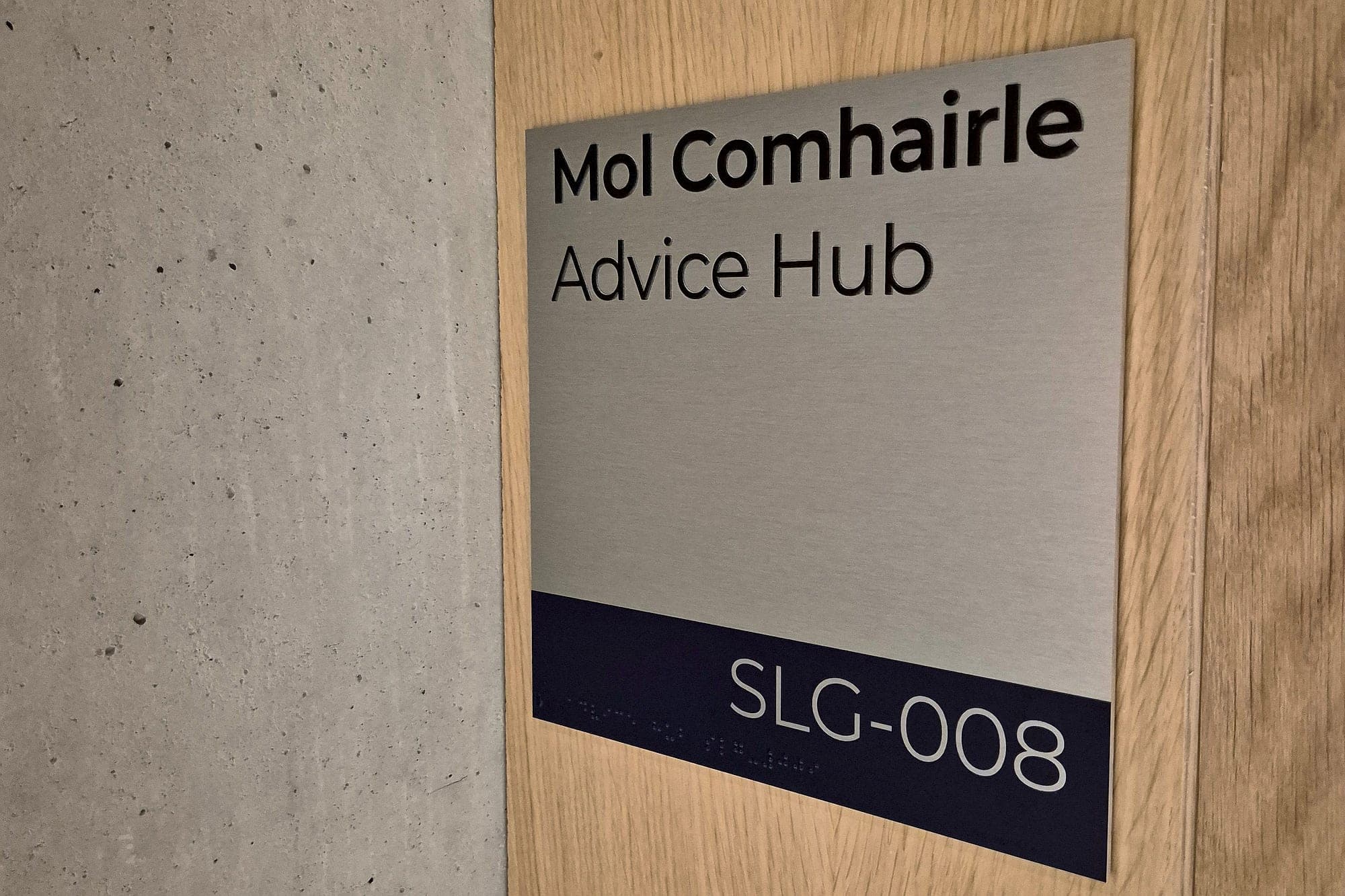Bilingual Irish and English door sign at the Glucksman Library, with raised tactile lettering, braille and the room code SLG-008 on a contrasting band