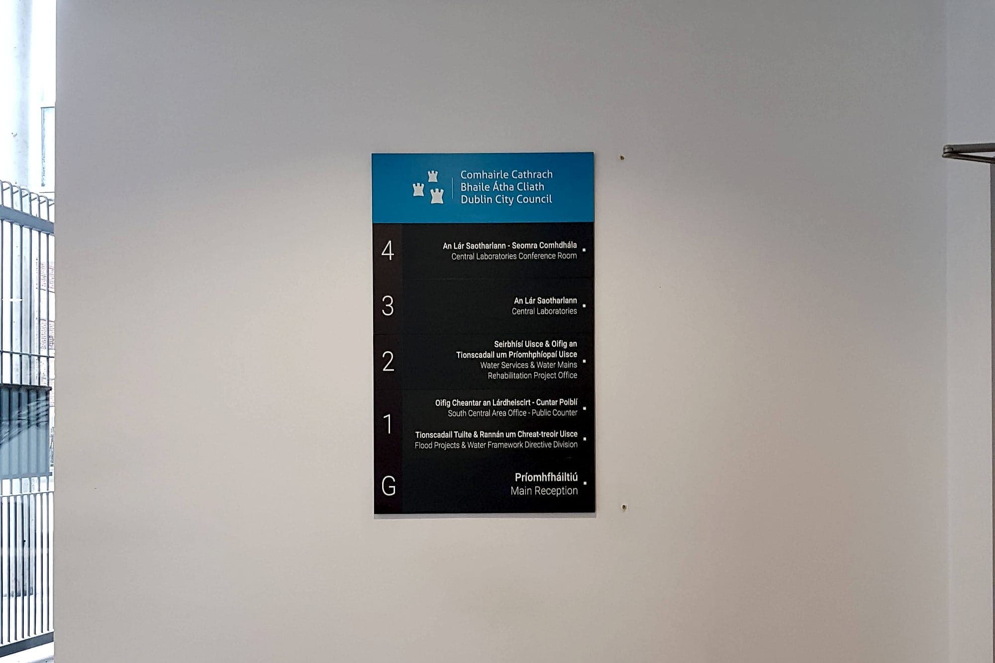 Bilingual Irish and English floor directory sign for Dublin City Council mounted in a lobby, listing departments by level from Ground to Fourth