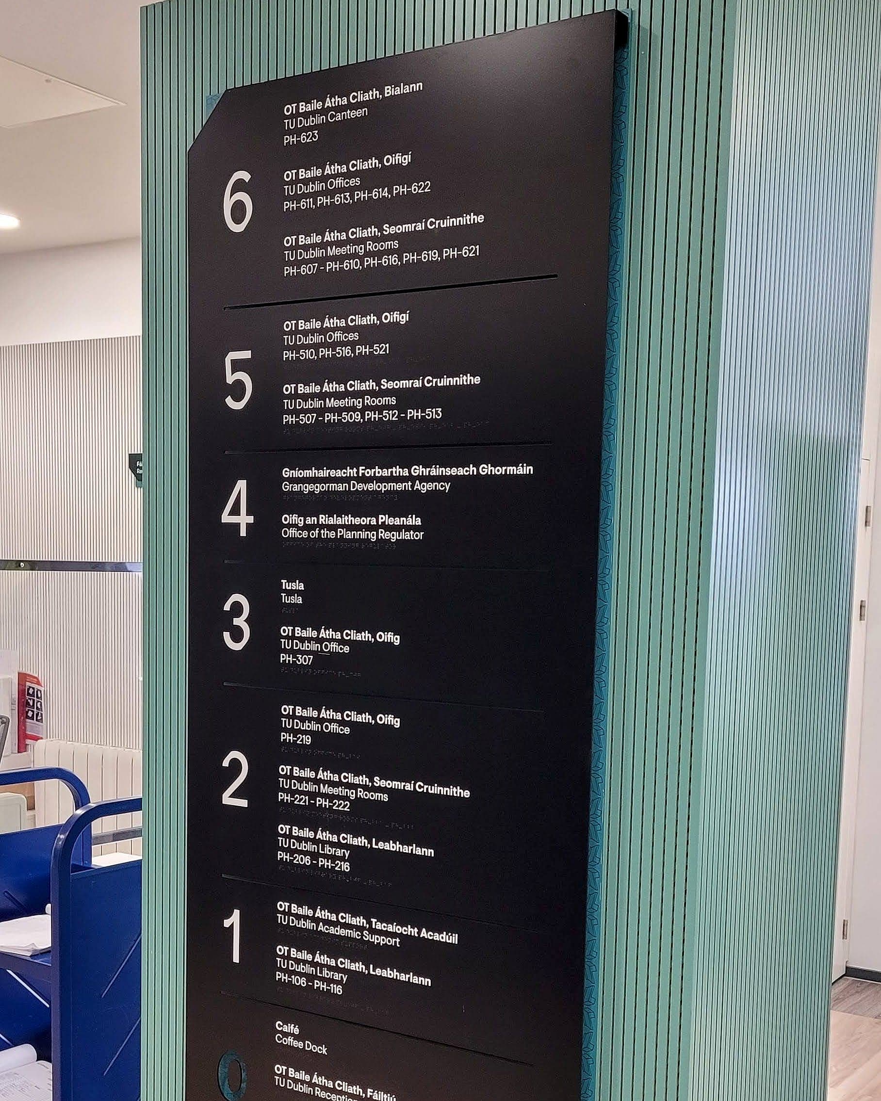 Bilingual Irish and English floor directory at Park House, TU Dublin, listing levels 6 to 1 with TU Dublin offices, meeting rooms and library alongside room codes such as PH-607 – PH-610 and PH-206 – PH-216, mounted on a green fluted panel