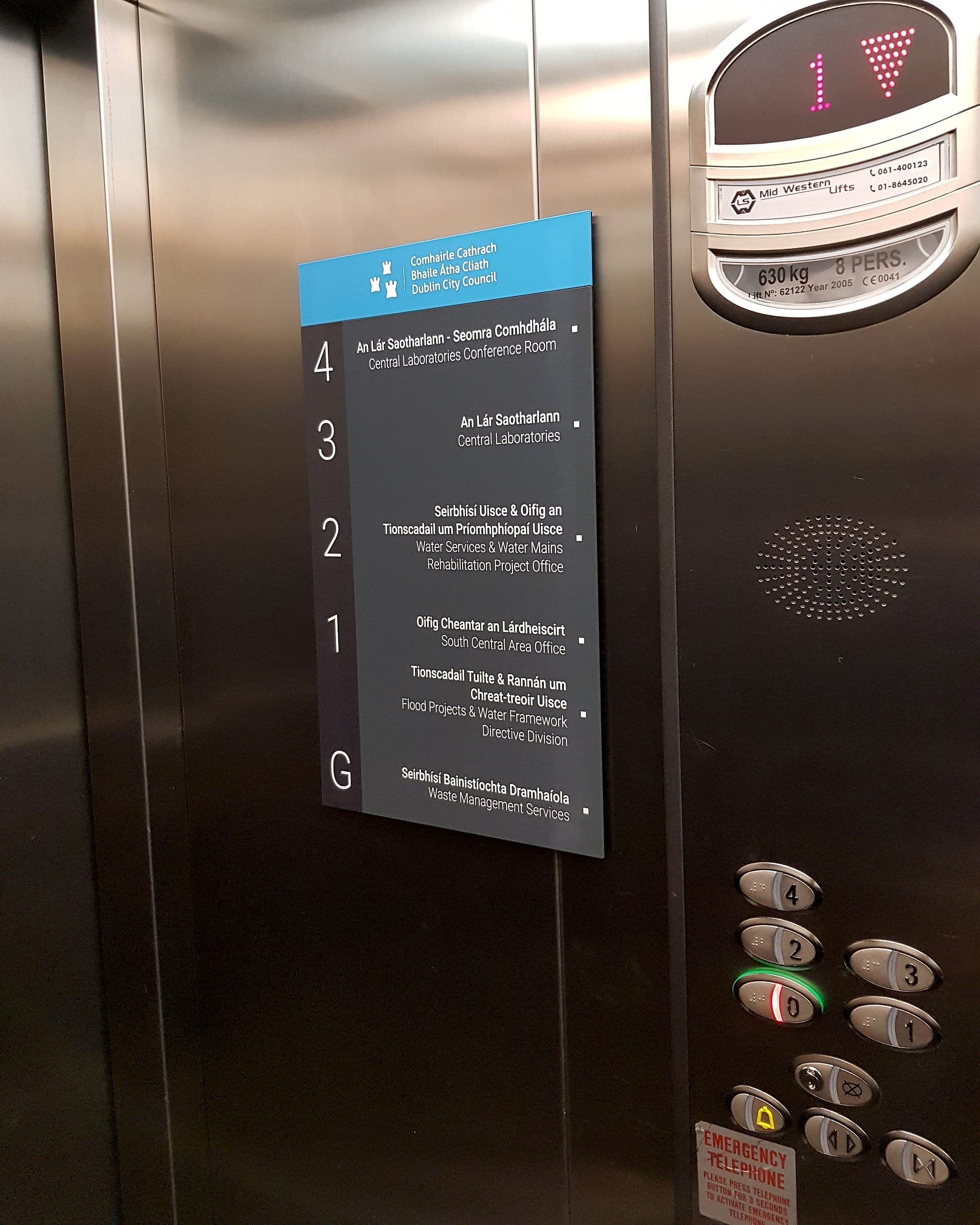 Eblana House: bilingual accessible floor directory inside a lift car in a Dublin City Council building, white mixed-case text on a dark panel listing departments level by level