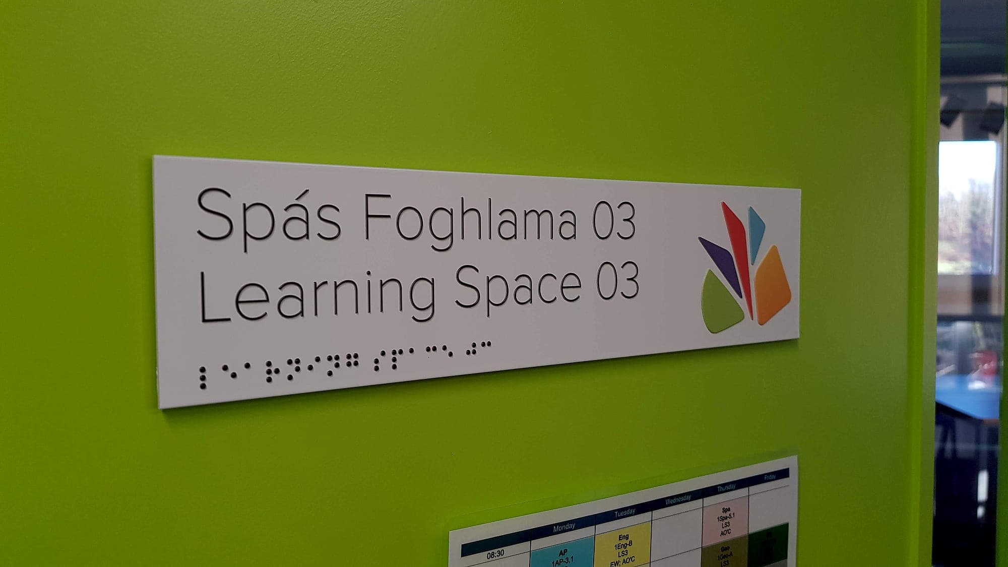 Ennistymon (BS 8300 signage in a school): bilingual tactile room sign with raised mixed-case lettering and braille on a white panel against a lime-green wall