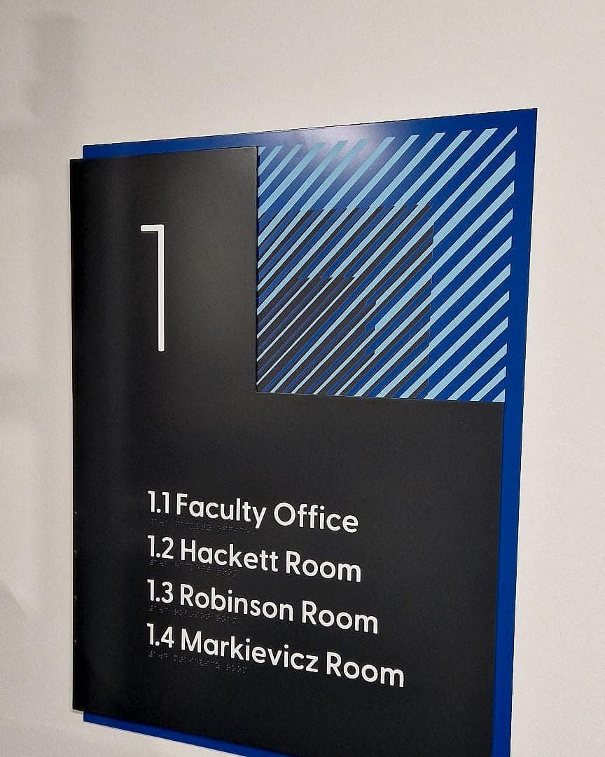 Floor directory at CCT College Dublin with braille beneath each line: level numeral 1 and four named rooms in white on a dark panel with a blue offset backing