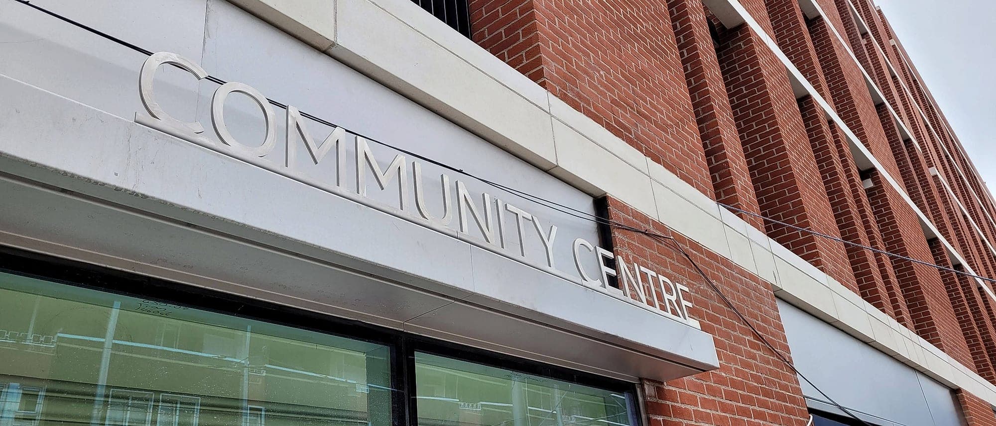 Dominic Street (accessibility audit finding): brushed metal lettering reading COMMUNITY CENTRE mounted on a brushed metal fascia, a light reflectance value contrast failure
