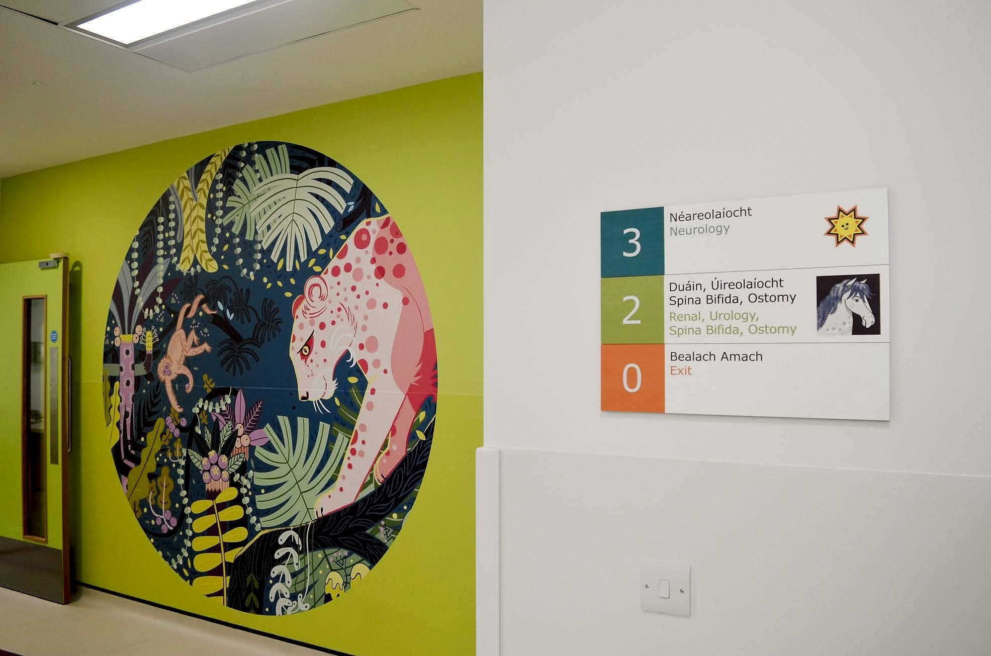 Calm jungle mural beside a symbol-coded bilingual floor directory at Temple Street Children's Hospital: landmark and autism friendly signage working together