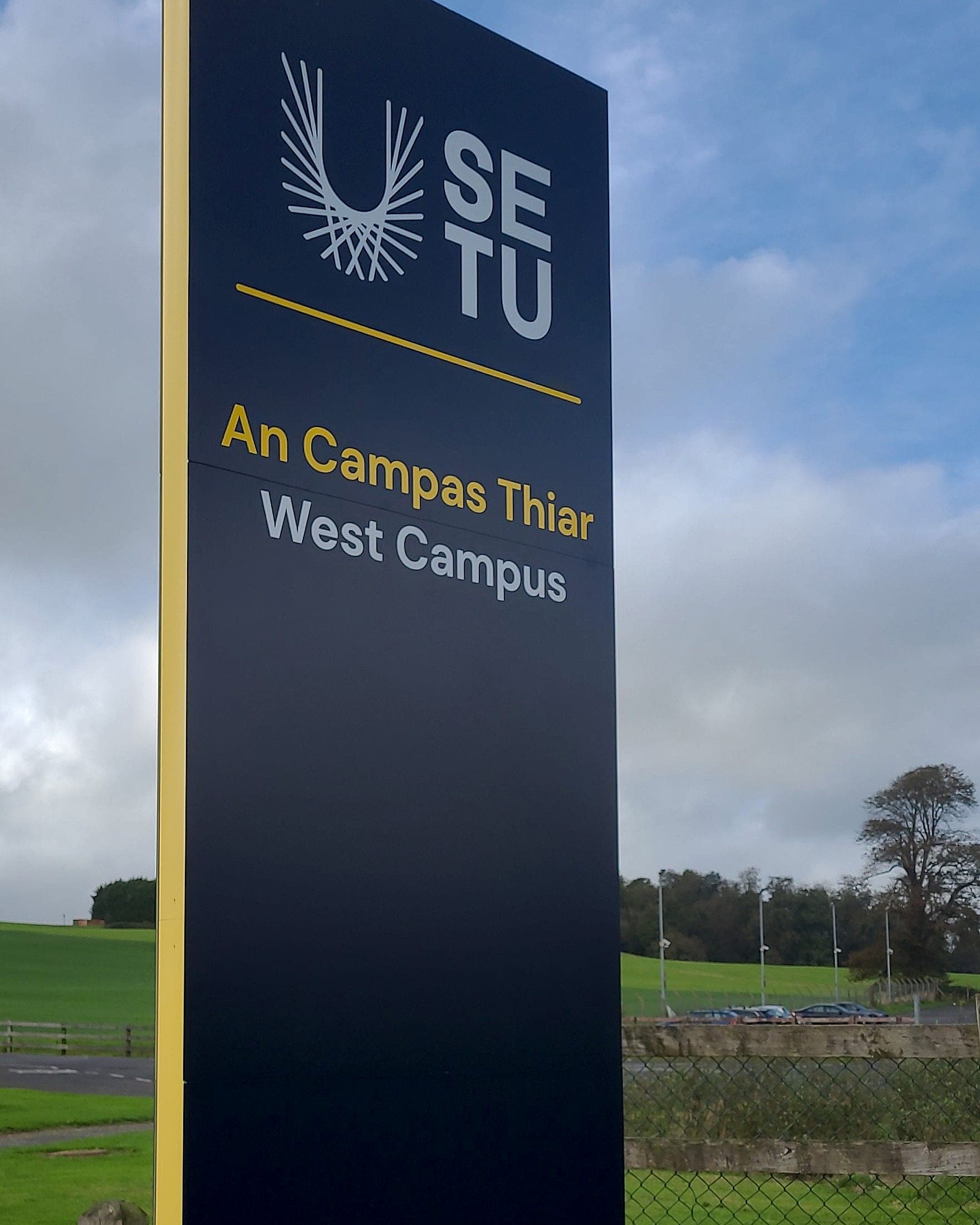 Navy and gold bilingual campus identity totem for South East Technological University West Campus, standing at the campus boundary