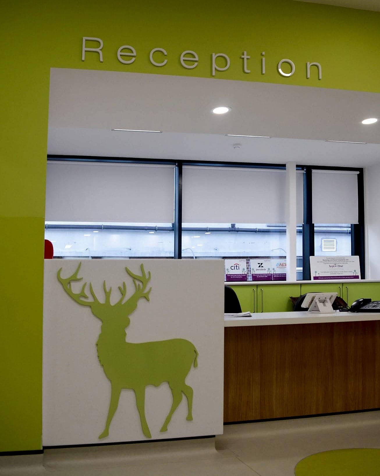 Reception at Temple Street Children's Hospital, Dublin: built-up Reception lettering on a lime green wall and a large cut stag silhouette on the desk end panel