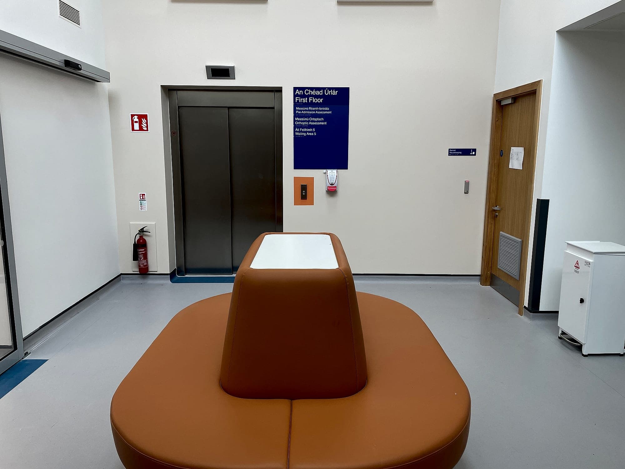 Lift lobby at South Infirmary Victoria University Hospital with bilingual level identification signage listing pre-admission assessment, orthoptic assessment and waiting area on the first floor