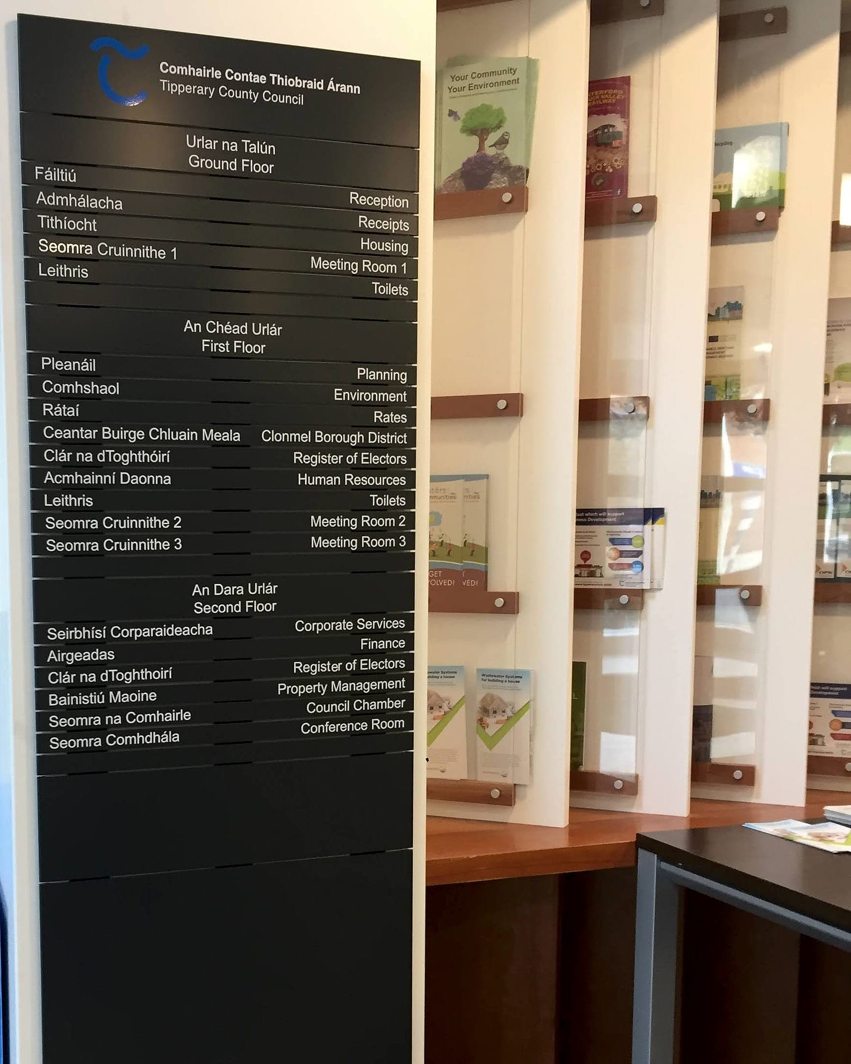 Council signage internal directory at Tipperary County Council's Clonmel District HQ: bilingual Irish and English floor-by-floor directory built from individual changeable slats listing Reception, Housing, Planning, Register of Electors and Council Chamber