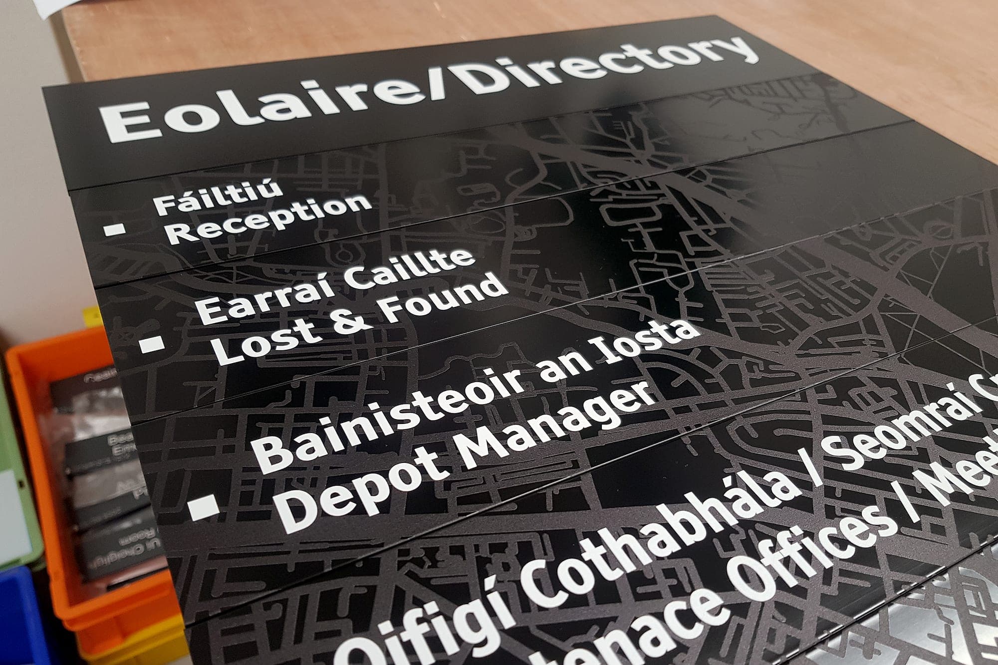 Bilingual Irish and English directory panels for Transport for Ireland laid out on the workbench before dispatch, reading Eolaire / Directory with Reception, Lost and Found, Depot Manager and Maintenance Offices over a street-map background graphic