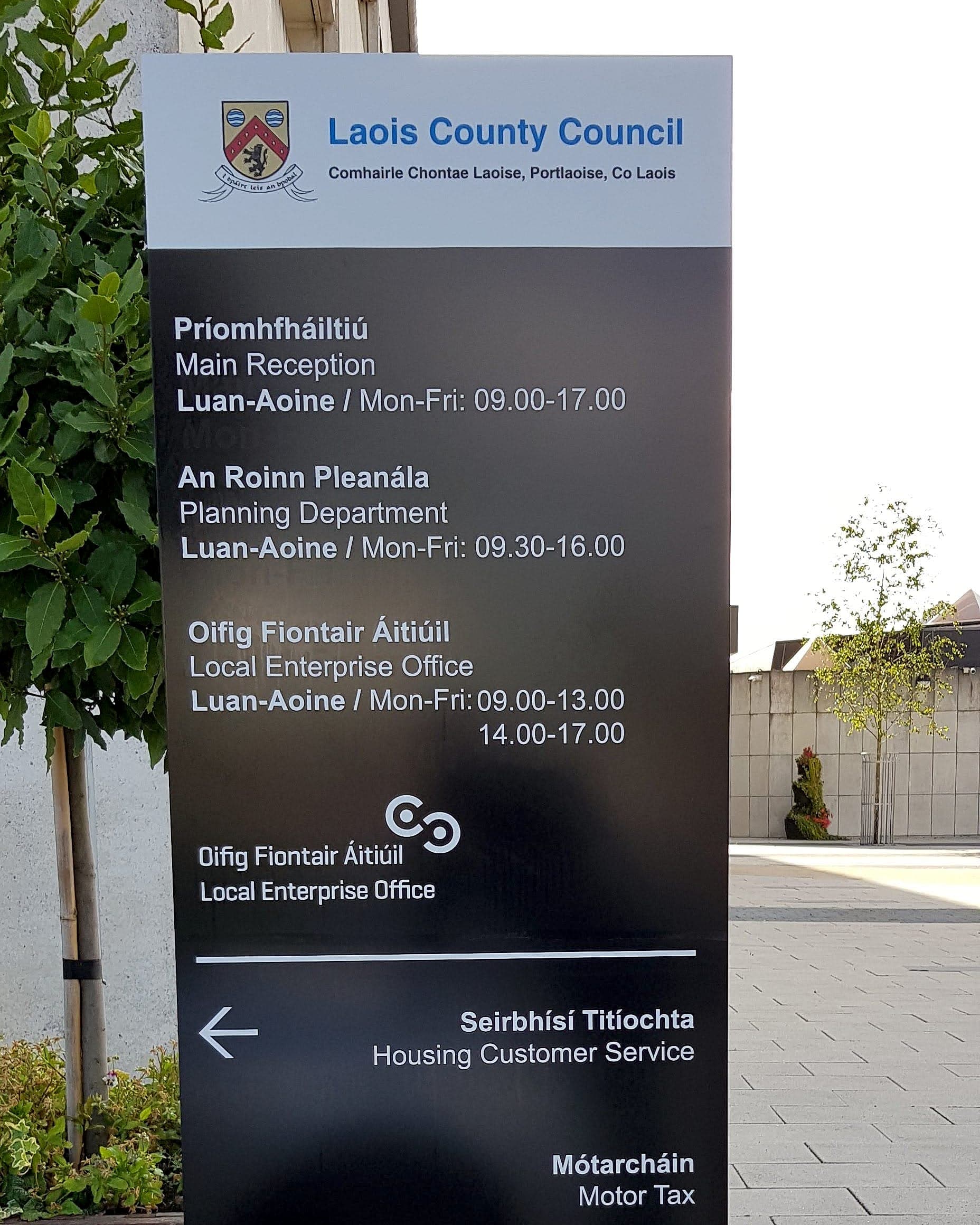 Council signage external totem at Laois County Council, Portlaoise: bilingual Irish and English directory listing Main Reception, Planning Department, Local Enterprise Office, Housing Customer Service and Motor Tax with opening hours
