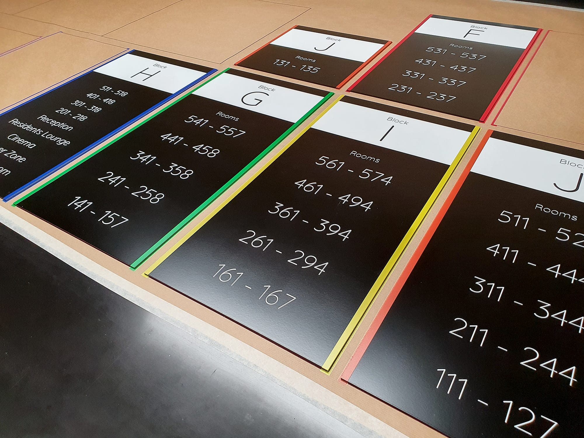Colour-coded block directory panels for Westwood Student Accommodation, Galway, laid out flat in the signage workshop before installation, each listing room-number ranges by floor