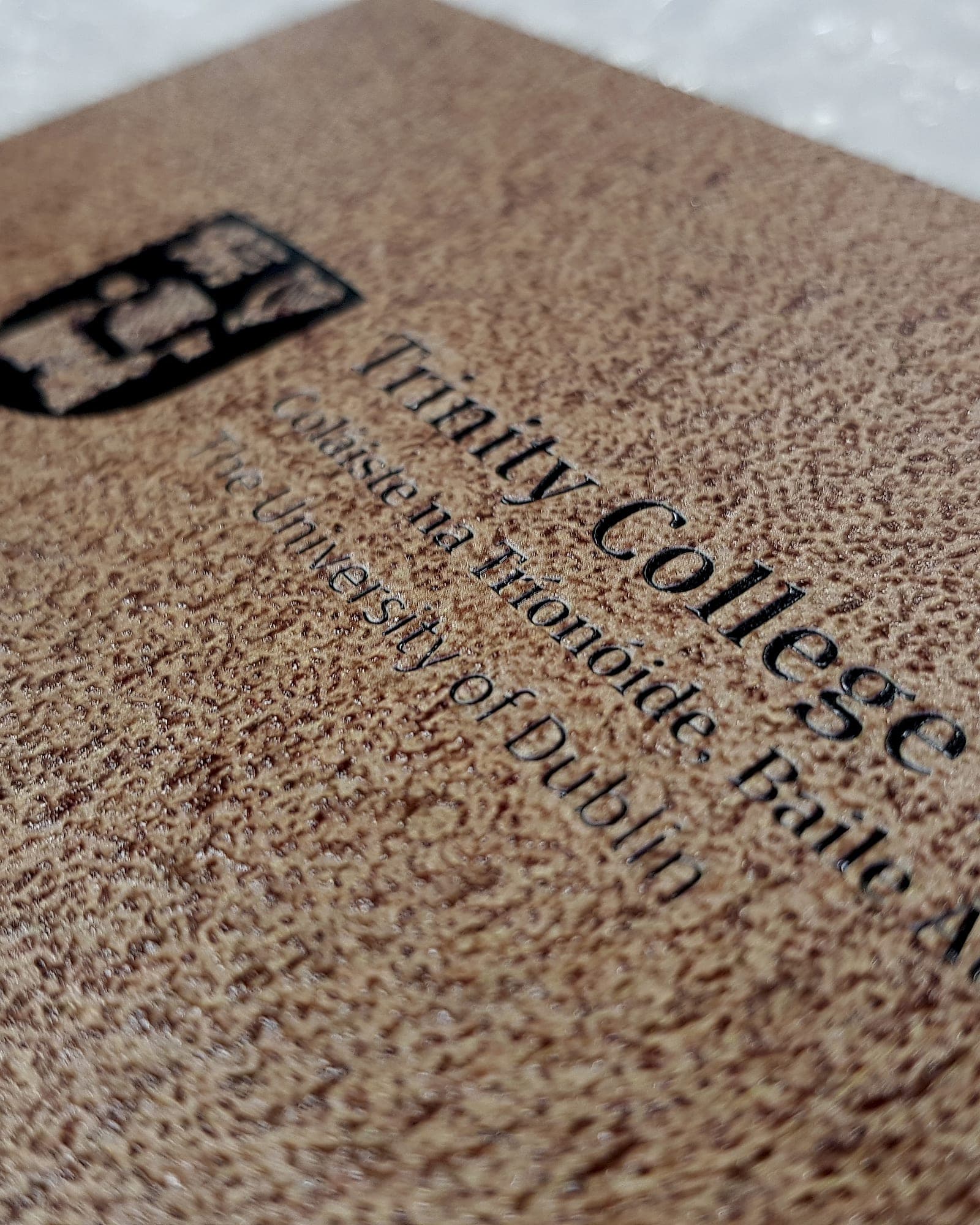A bronze-finish bilingual Trinity College Dublin plaque with the college crest and engraved Irish and English lettering, photographed on protective wrapping before dispatch