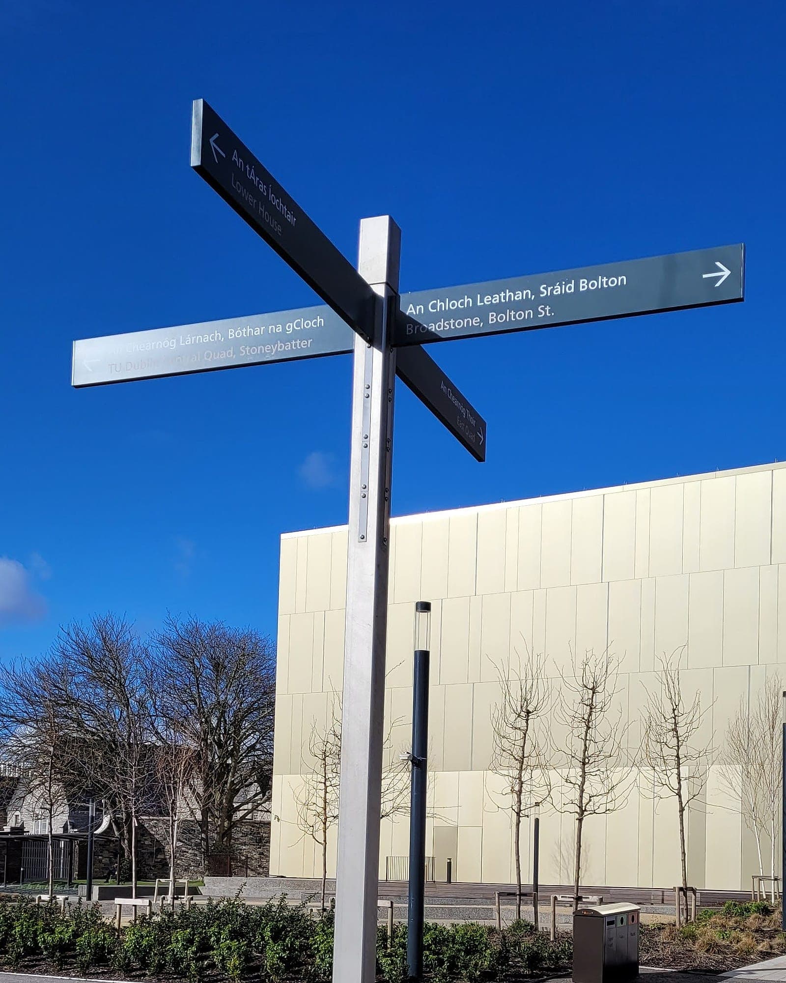 TU Dublin Grangegorman: bilingual four-arm fingerpost at a path junction on an estate, naming buildings on the grounds and streets beyond