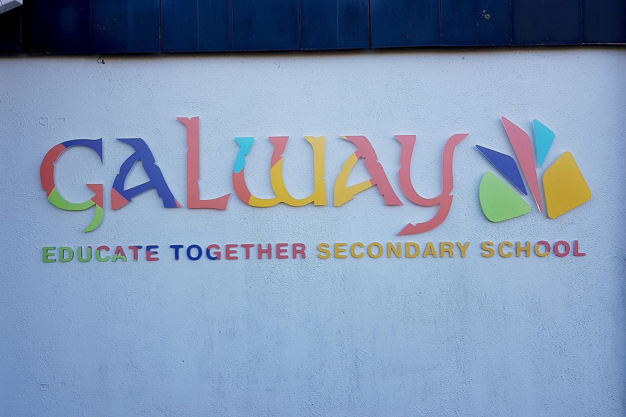 External lettering durability: multi-coloured flat-cut acrylic building identification lettering, printed direct to the face, for Galway Educate Together Secondary School fixed directly to a rendered external wall