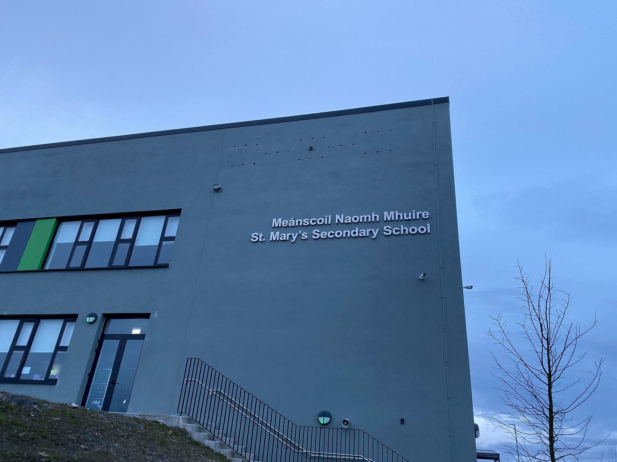 External building identification lettering high on a rendered gable at St Mary's Secondary School, bilingual Irish and English, photographed at dusk, a Department of Education project