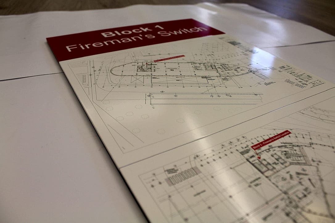 A statutory sign and the drawing that places it: a statutory fireman's switch sign in red and white lying on fire strategy drawings that mark its location on the building plan