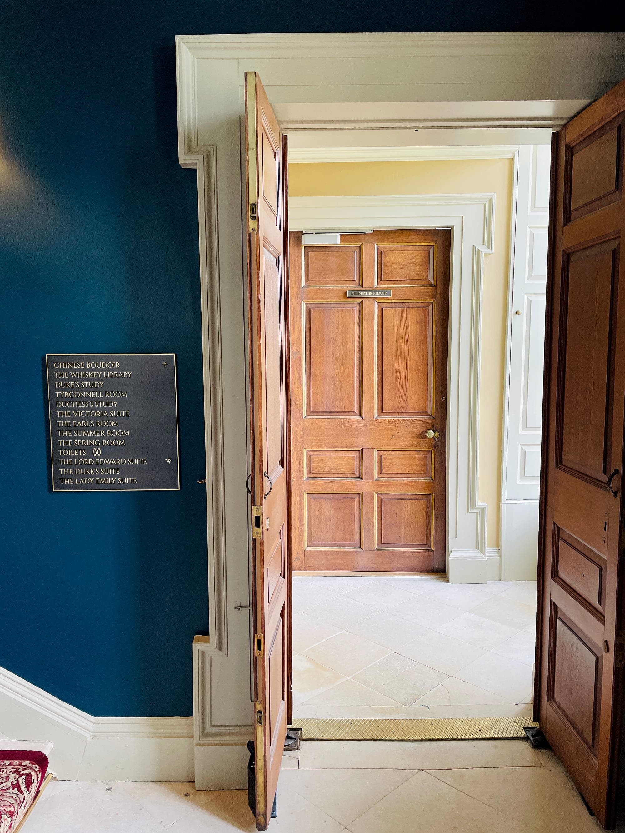 Brass-lettered directory sign on a deep blue wall at Carton House hotel, listing named suites and rooms beside a Georgian doorway