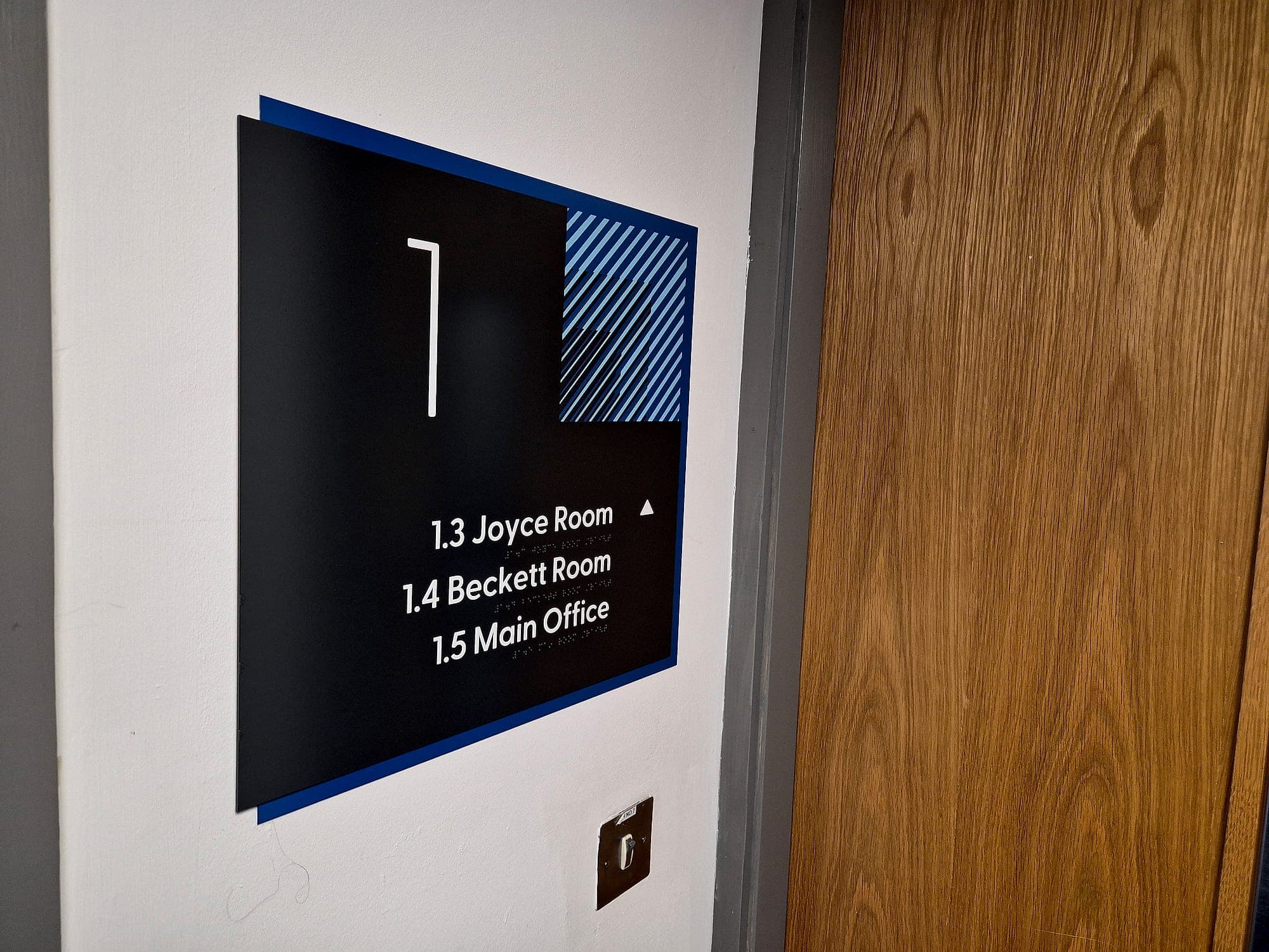 High-contrast floor-level directional sign at CCT College's Westmoreland Street campus, at a corridor decision point listing room numbers and names with a directional arrow