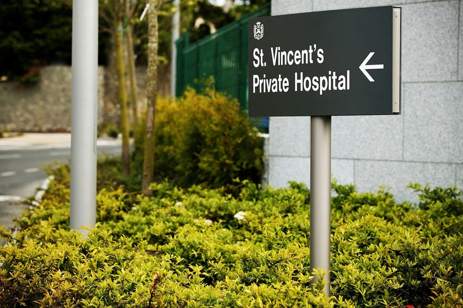External directional hospital signage at St Vincent's Private Hospital, Dublin: post-mounted panel with arrow at the site entrance