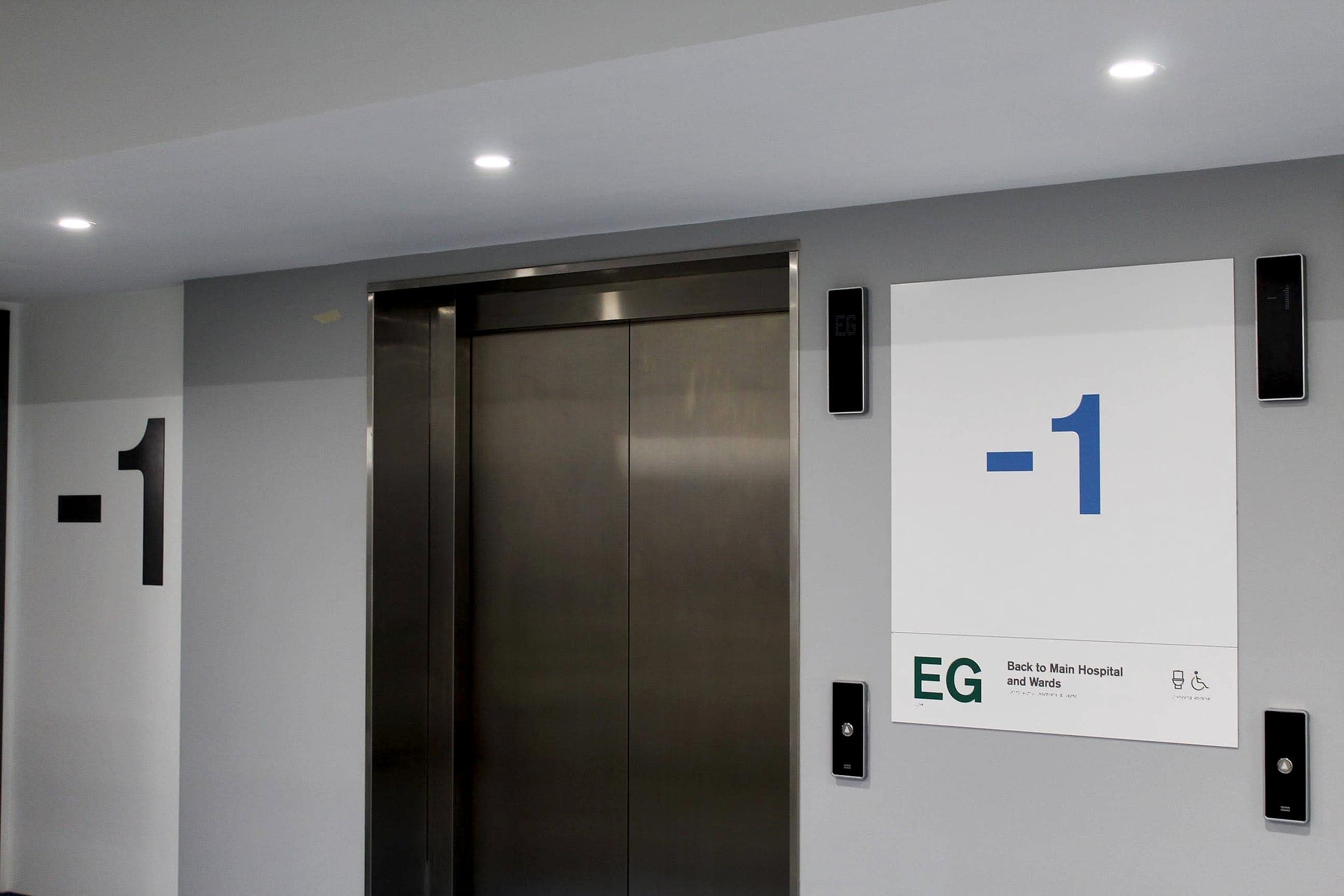 Hospital wayfinding at the National Rehabilitation Hospital: oversized floor-level supergraphic beside lifts, with a compliant tactile and braille lift-lobby sign
