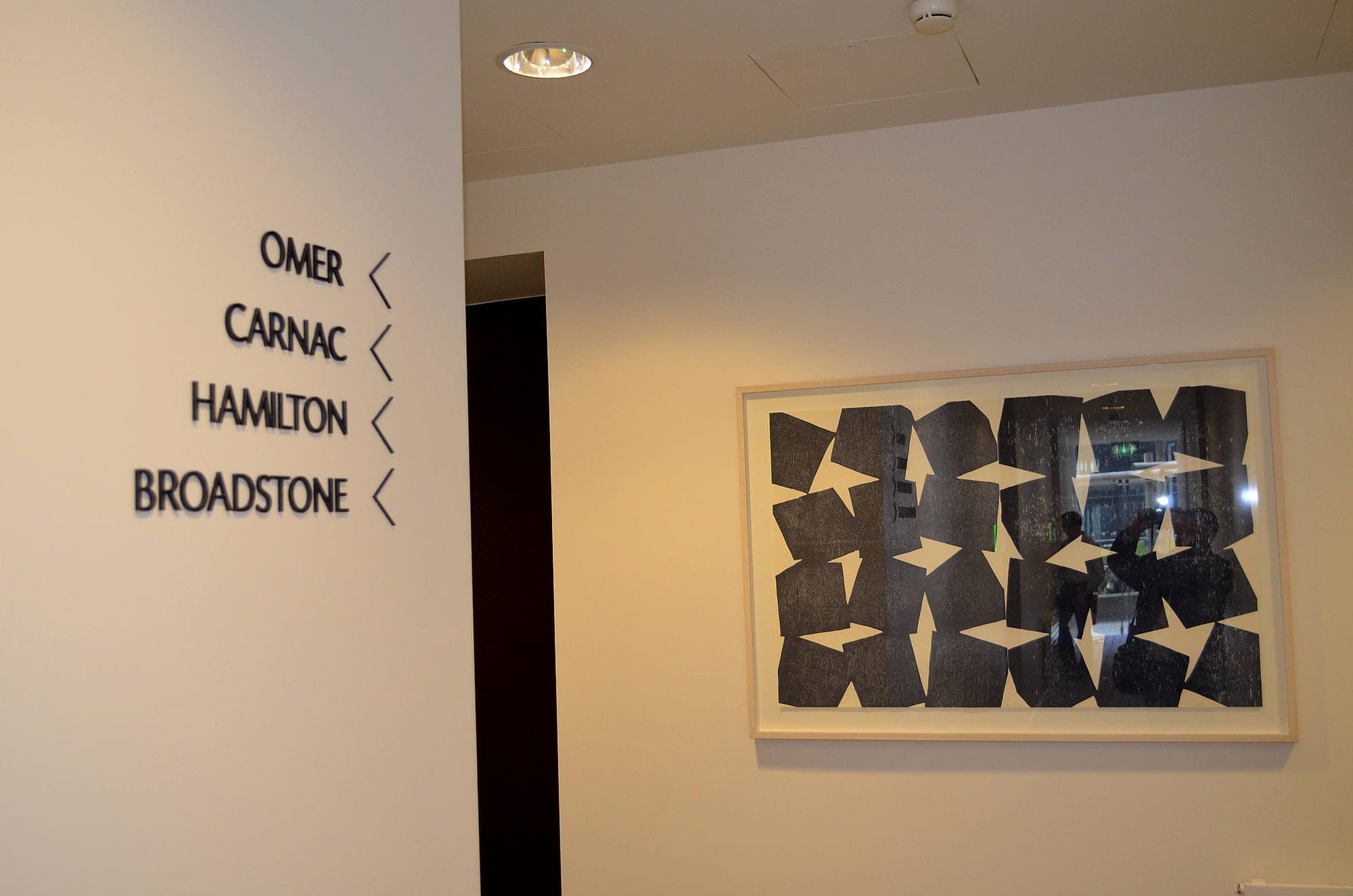 Hotel signage in a corridor at The Marker Hotel, Dublin: flat-cut black lettering listing named rooms with directional chevrons, beside a framed artwork
