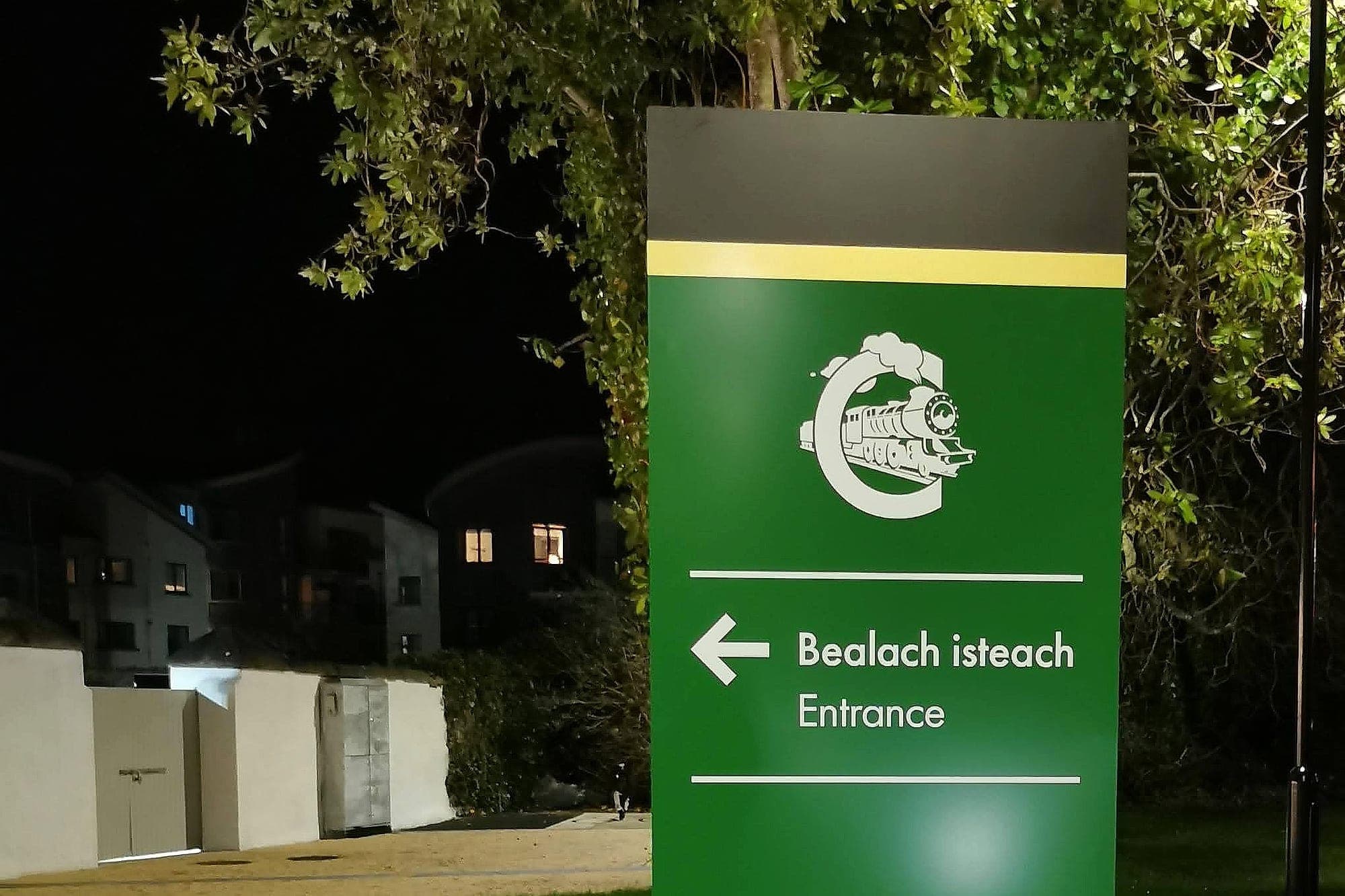 Illuminated bilingual entrance totem at the Railway Museum, Malahide, photographed at night on the grounds and lit by a nearby luminaire