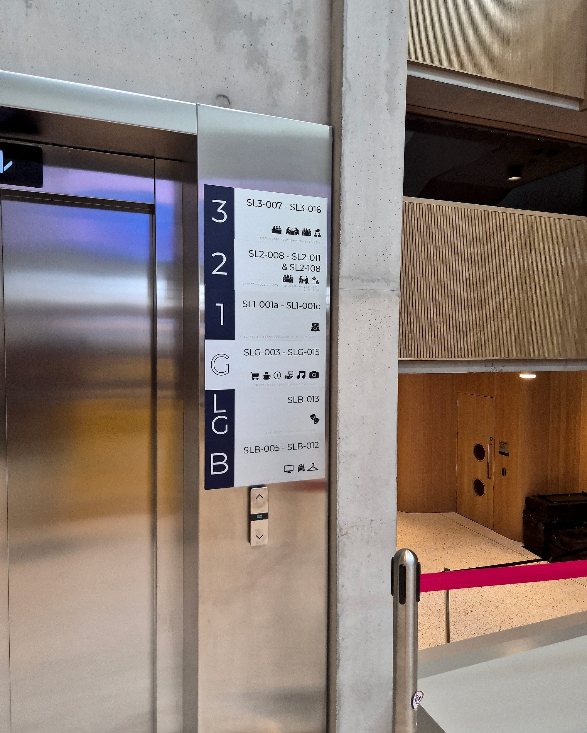Modular internal signage strip beside a lift at the UL Student Union: a vertical floor directory built as separate bands, each floor number paired with its room-number range and pictograms