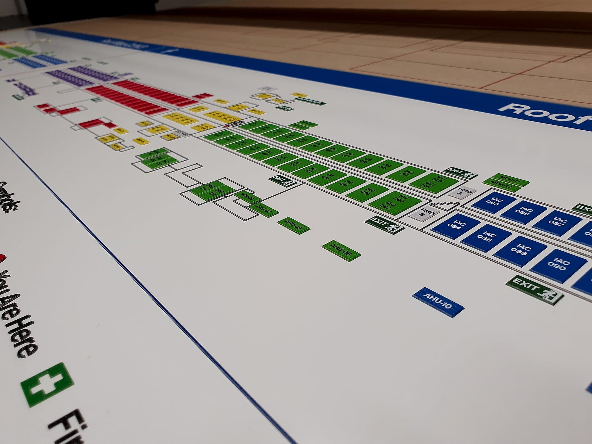 Sign manufacturing: a large-format printed wayfinding floor plan laid flat on a workshop table, showing colour-coded rooms, exit symbols and a You Are Here marker before trimming